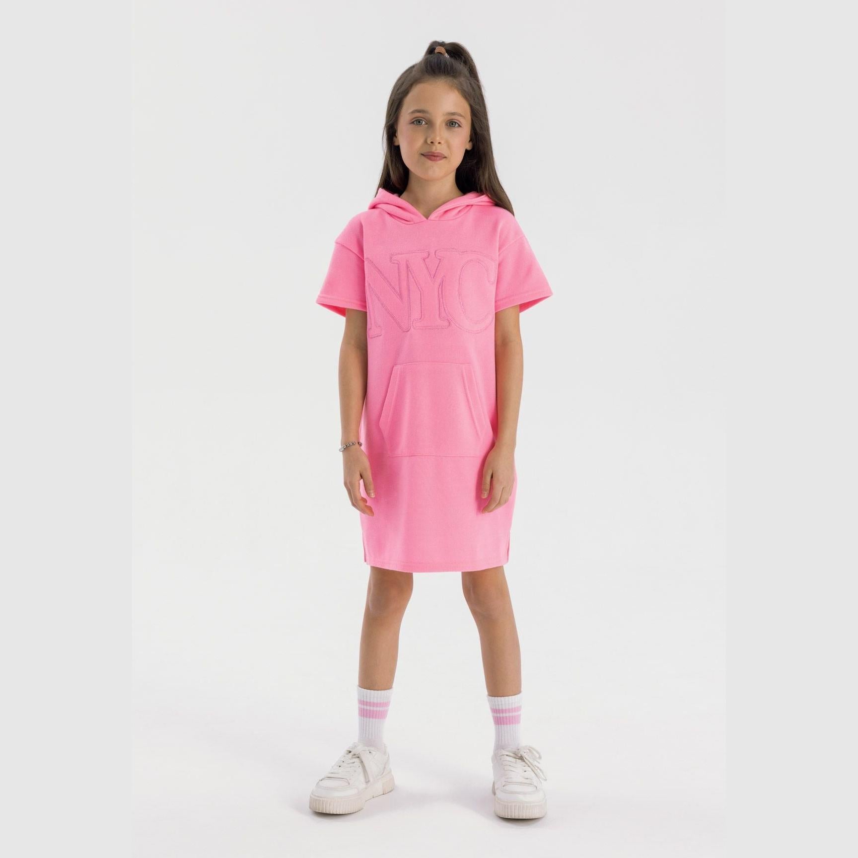 Girl wearing pink cotton fleece hooded dress with NYC embroidery, white socks and sneakers on light background