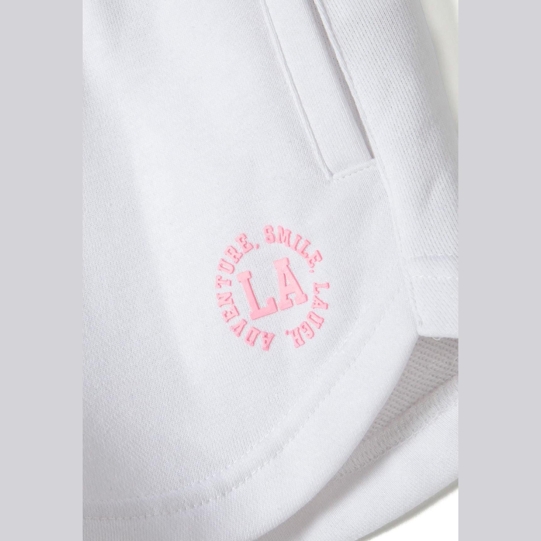 Close-up detail of white shorts showing pink circular L.A. logo with 'SMILE' text around the border