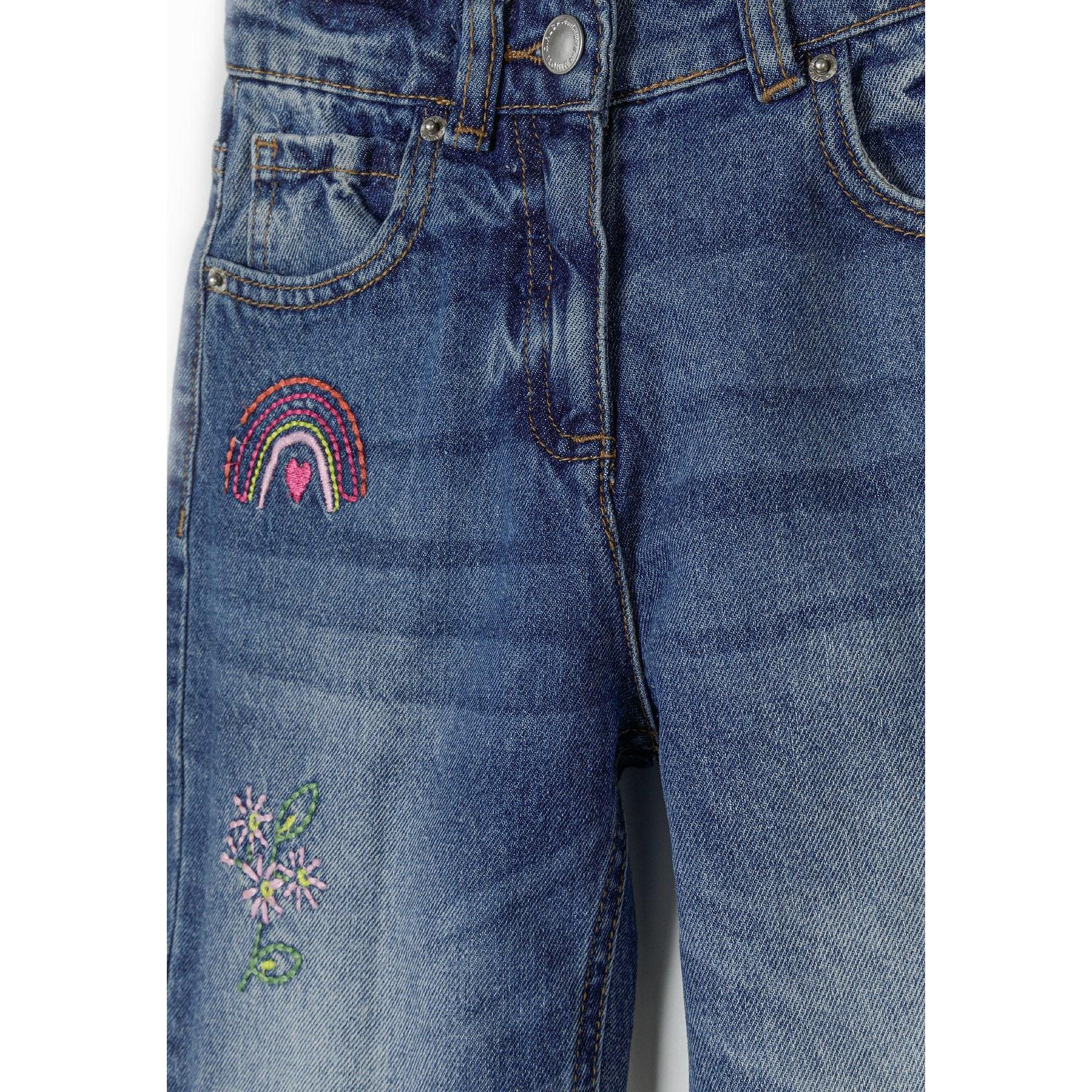 Close-up detail of navy jeans front showing rainbow and floral embroidery with classic denim construction and button fastening