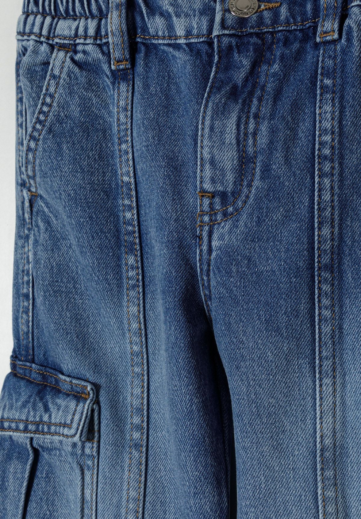 Close-up detail of navy denim cargo jeans showing front waistband, button closure and cargo pocket construction