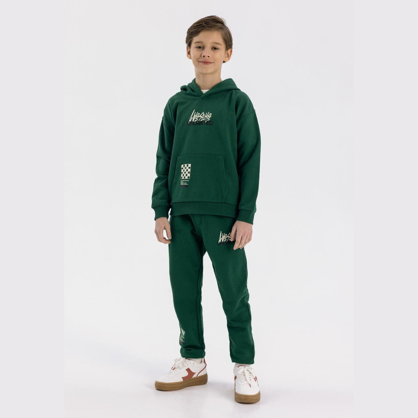 Boy wearing green fleece tracksuit set with Awesome Unlimited print, featuring hoodie and joggers, standing against white background