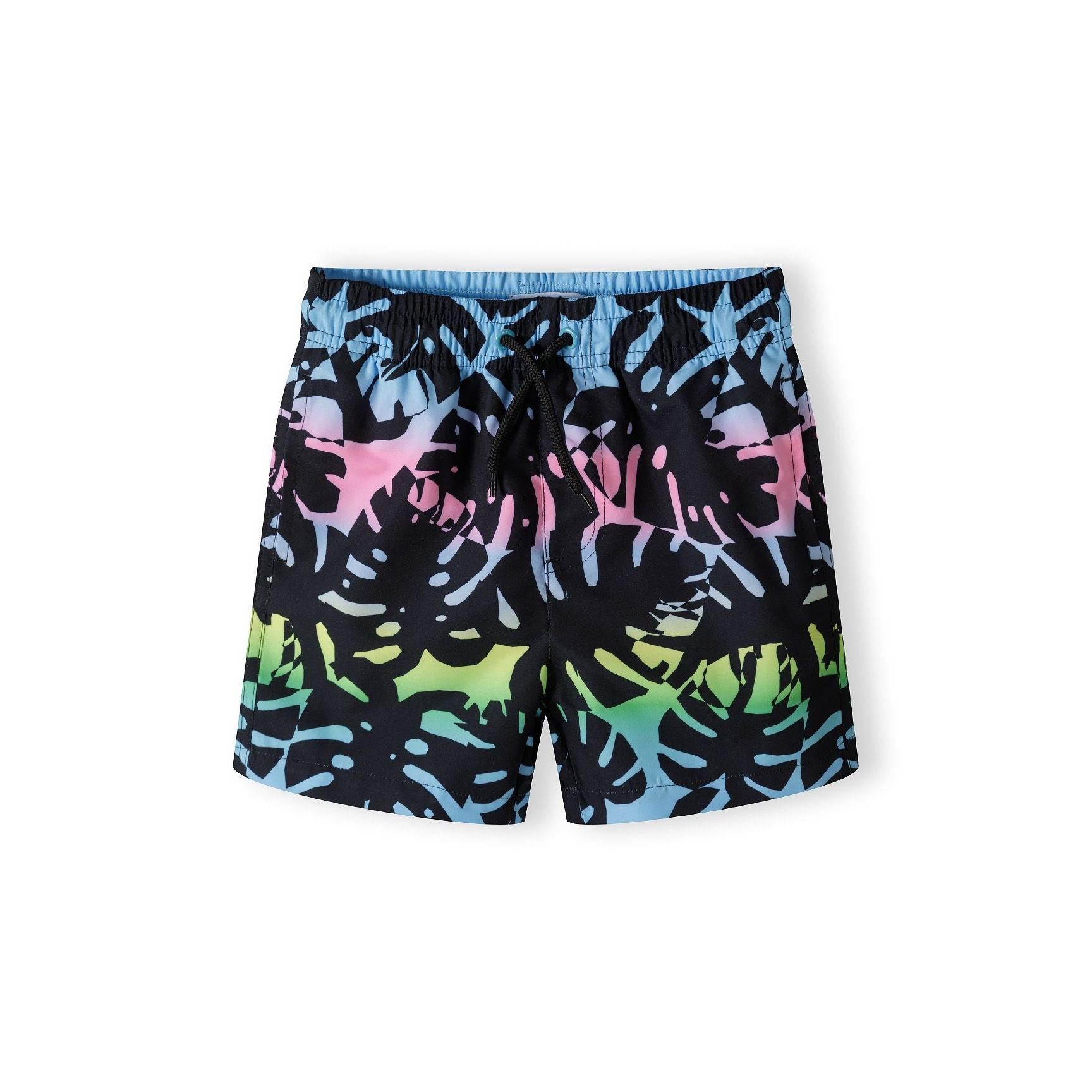 Front view of black board shorts with vibrant tropical monstera leaf print in gradient colors from blue to pink to green, featuring elastic waistband with drawstring on white background