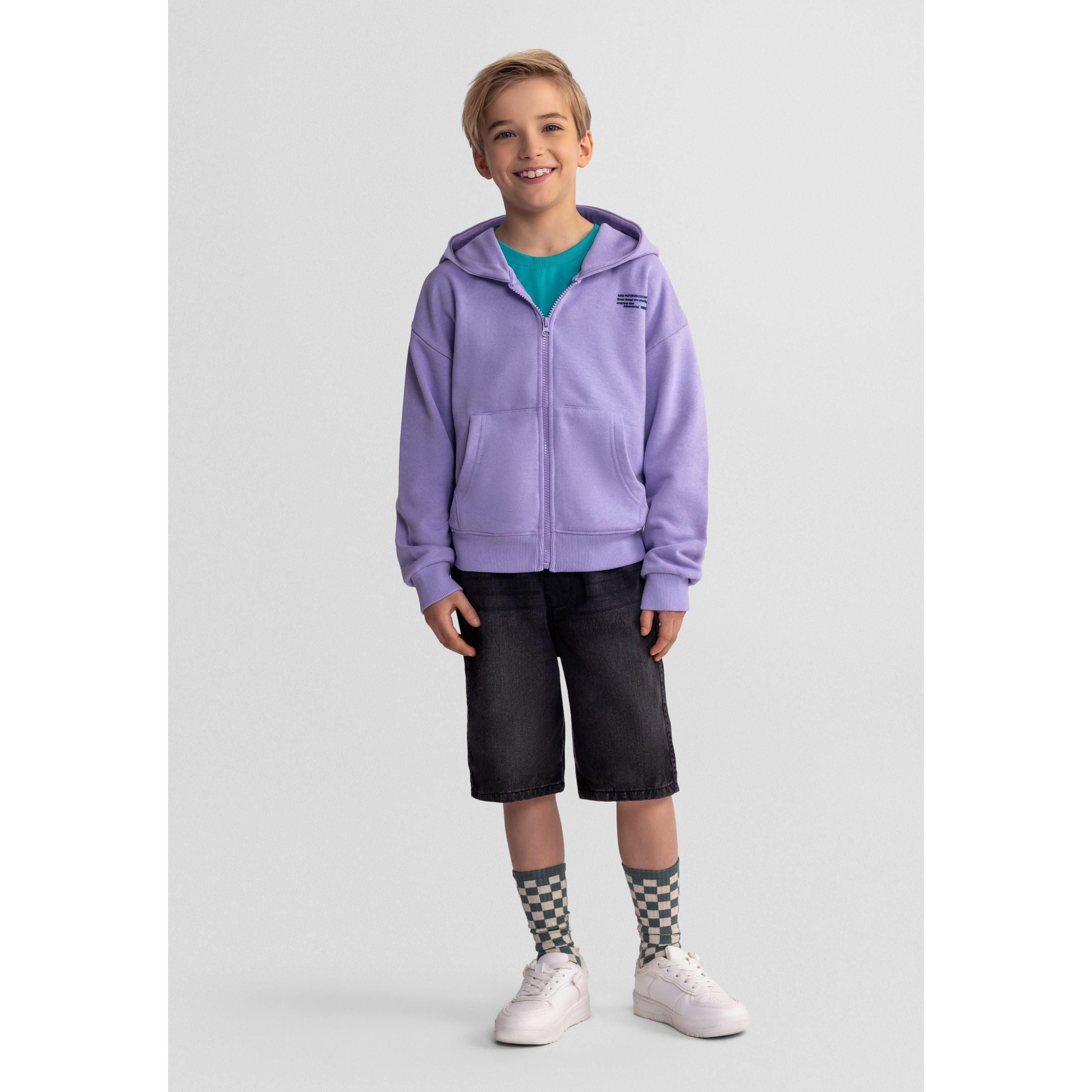 Young boy wearing purple zip-up hoodie over teal t-shirt with dark denim shorts and checkered socks, standing against white background