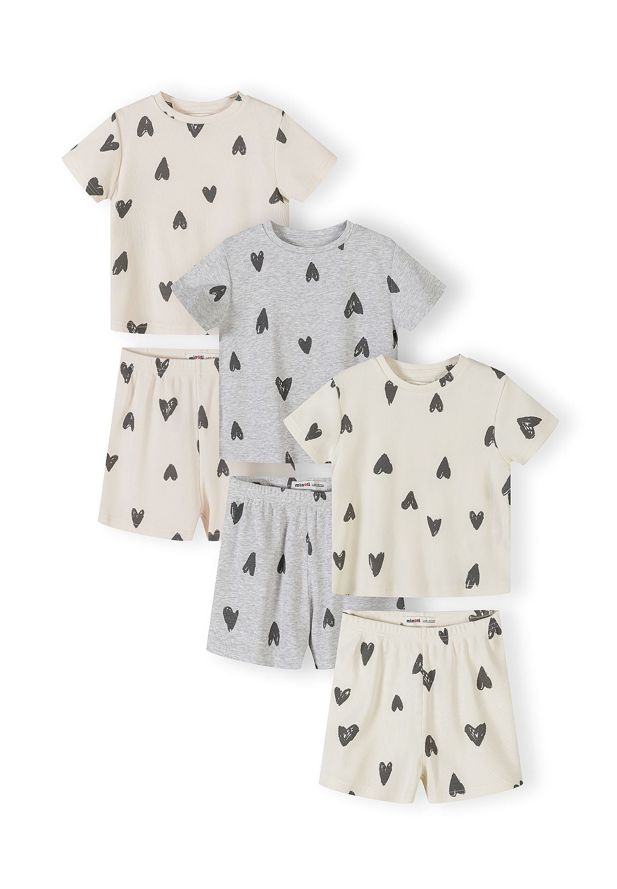 Six ribbed cotton pyjama pieces laid flat showing three complete sets in cream and grey with black hearts print pattern