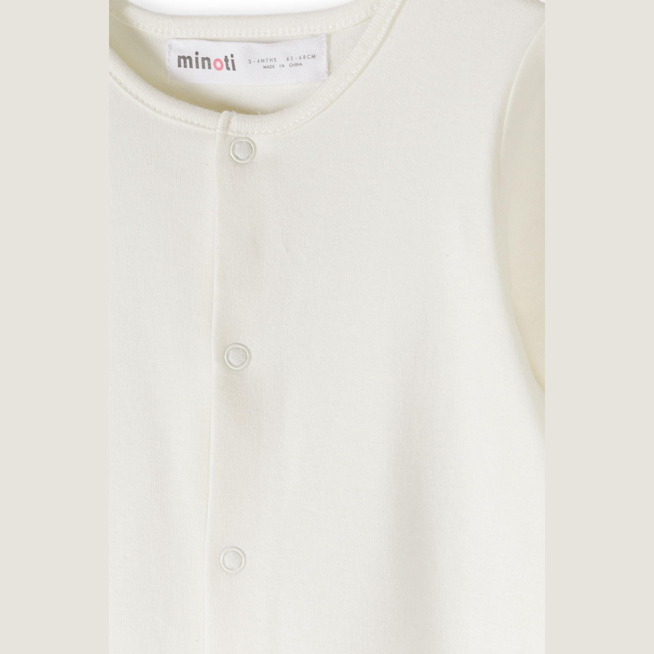 Close-up detail of cream sleepsuit showing Minoti label, snap button closures and ribbed neckline construction