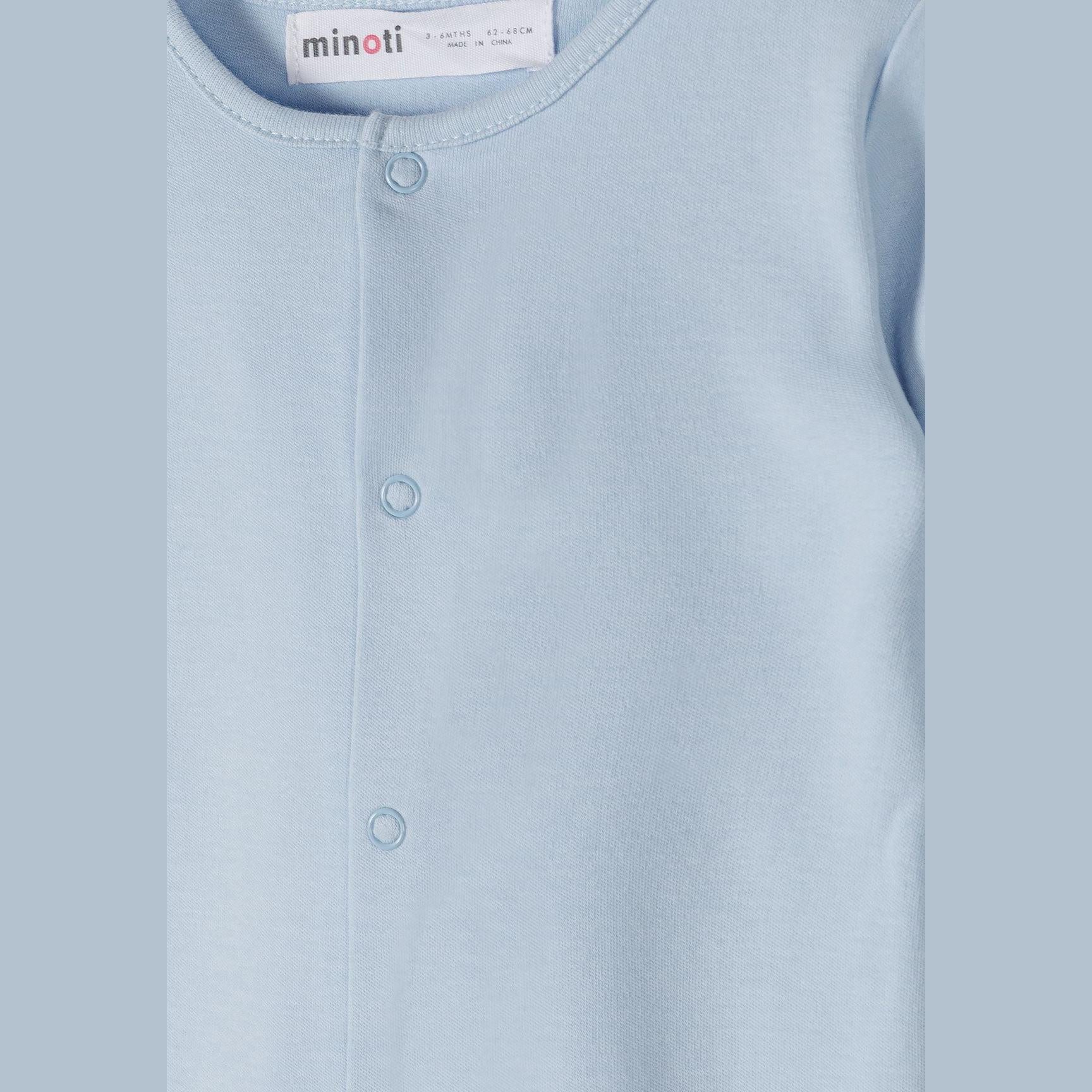 Close-up detail of light blue sleepsuit showing Minoti label, snap button closure and ribbed collar construction