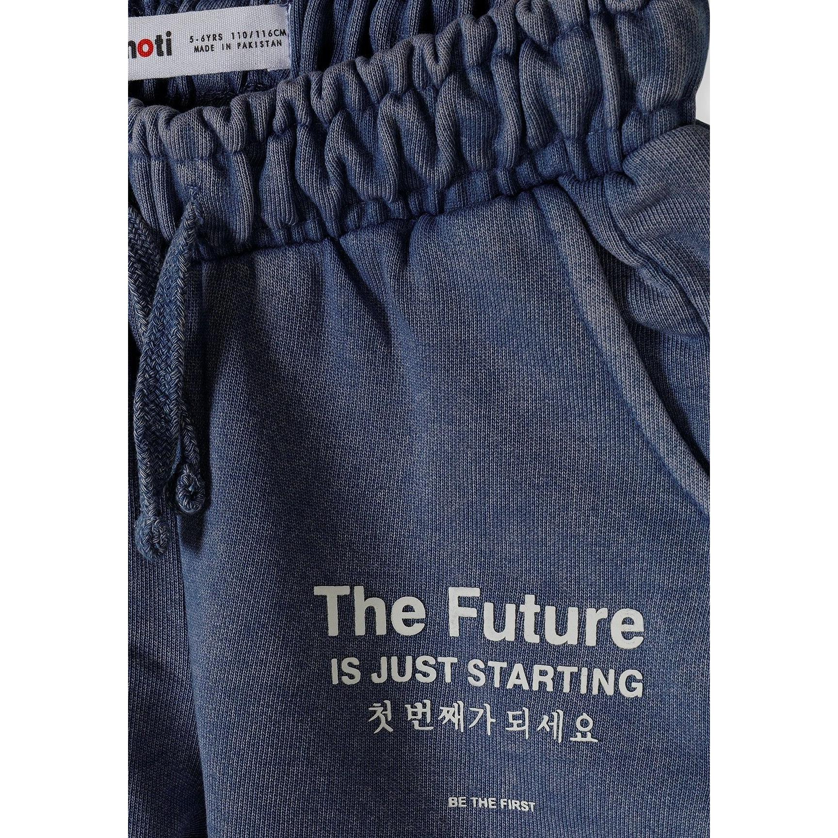 Close-up detail of blue acid wash shorts waistband showing Minoti label and 'The Future is Just Starting' text with Korean translation