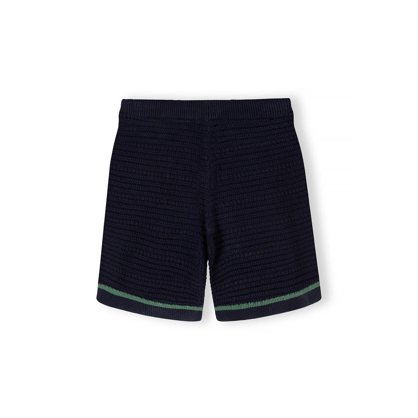 Close-up detail of navy blue knitted polo shirt showing Minoti label, button placket, chest pocket with green piping trim