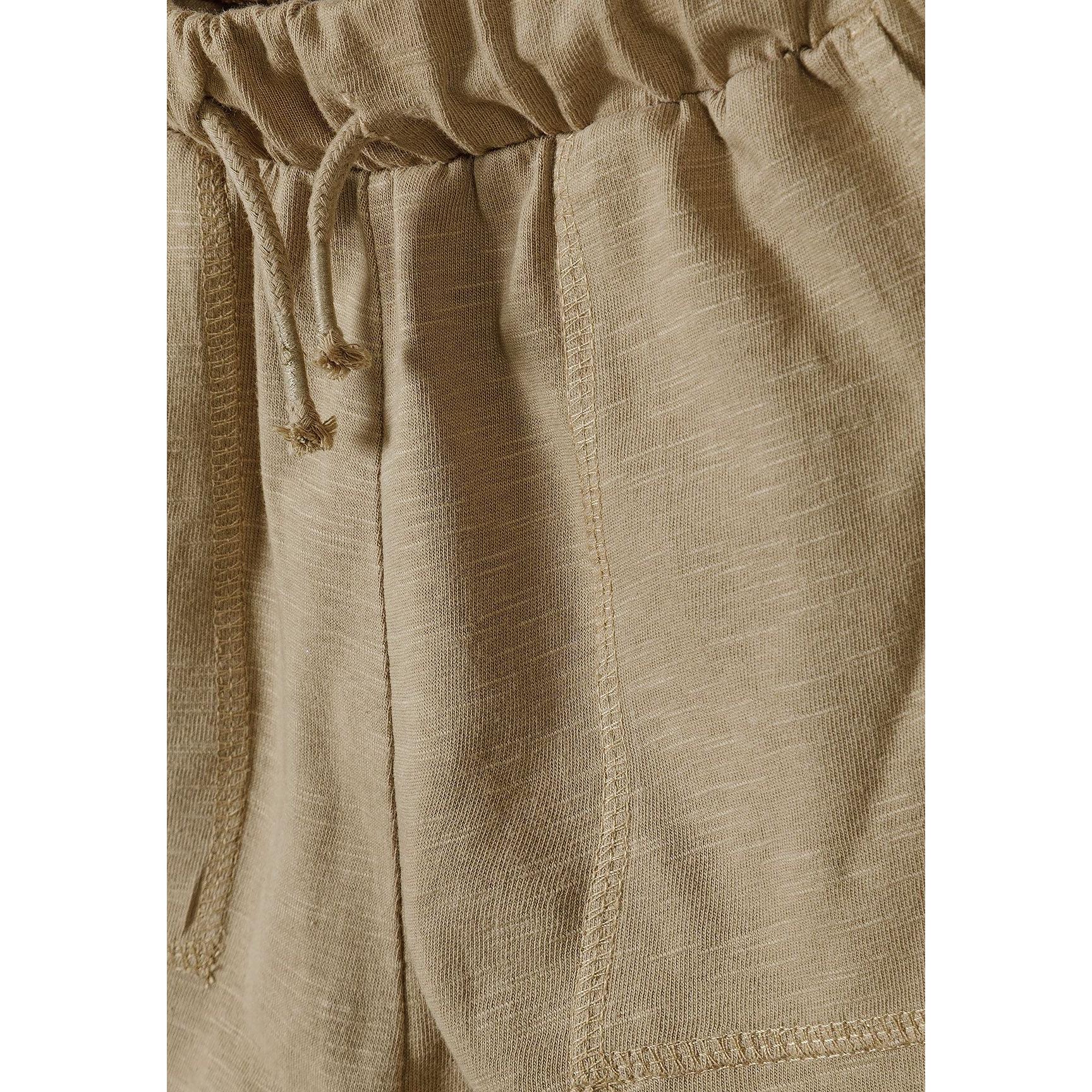 Close-up detail of camel shorts showing elasticated waistband with toggle drawstring closure and fabric texture