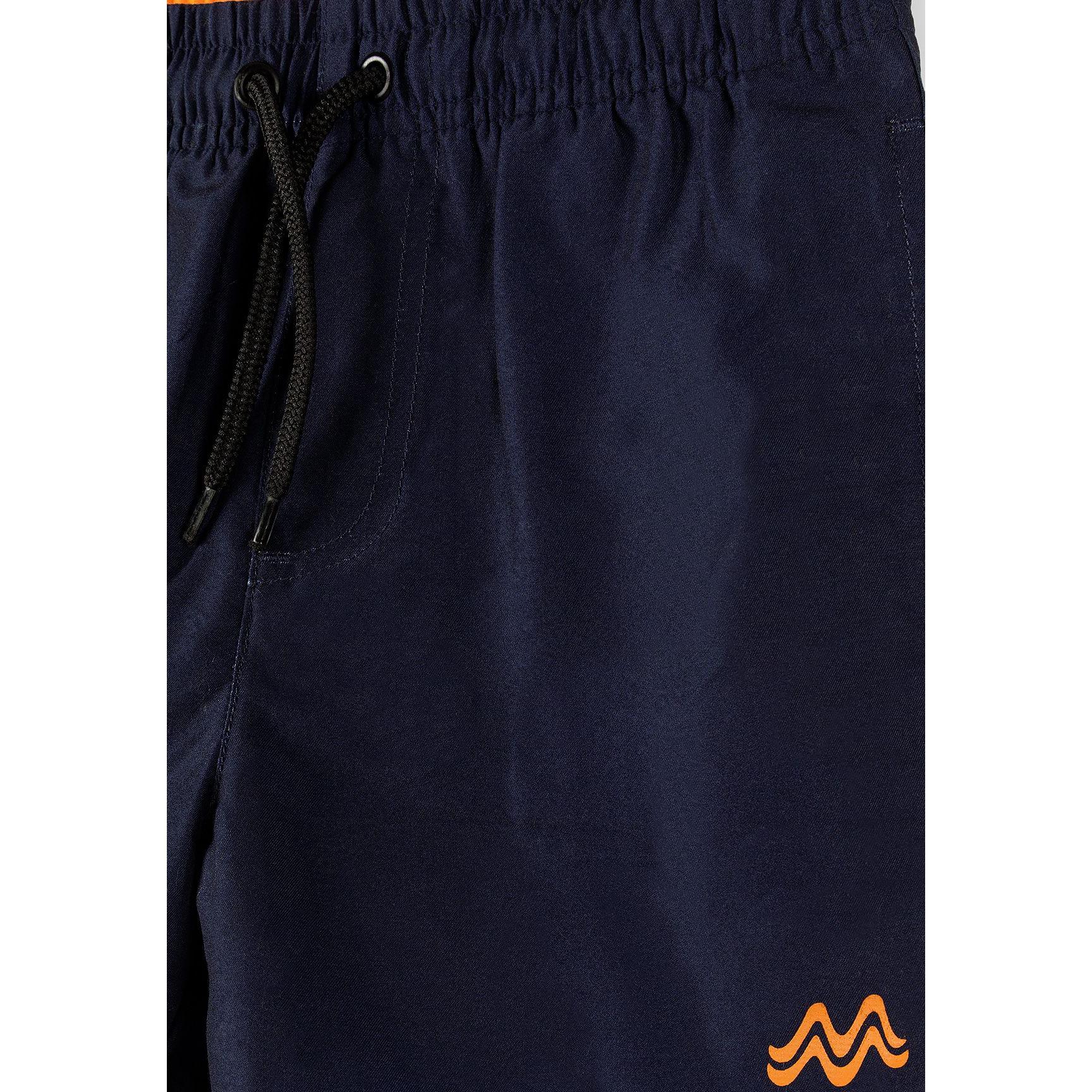 Close-up detail of navy swim shorts showing drawstring ties, elastic waistband and orange logo embroidery