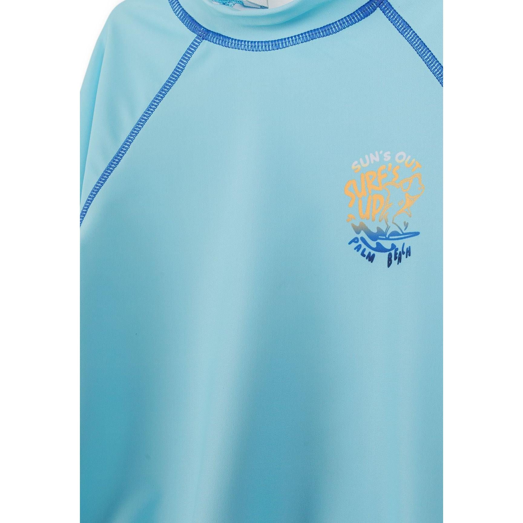 Close-up detail of solid light blue swim t-shirt showing chest print with text and wave design, blue contrast stitching visible around neckline