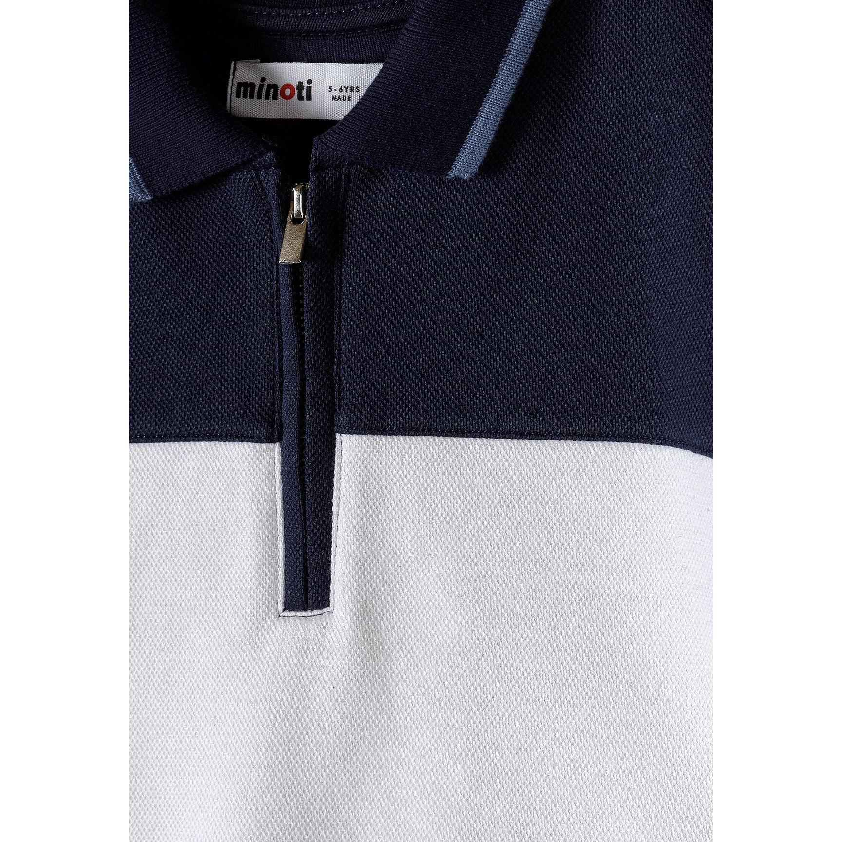 Close-up detail of Minoti label and zip collar on navy and white pique polo shirt showing textured fabric