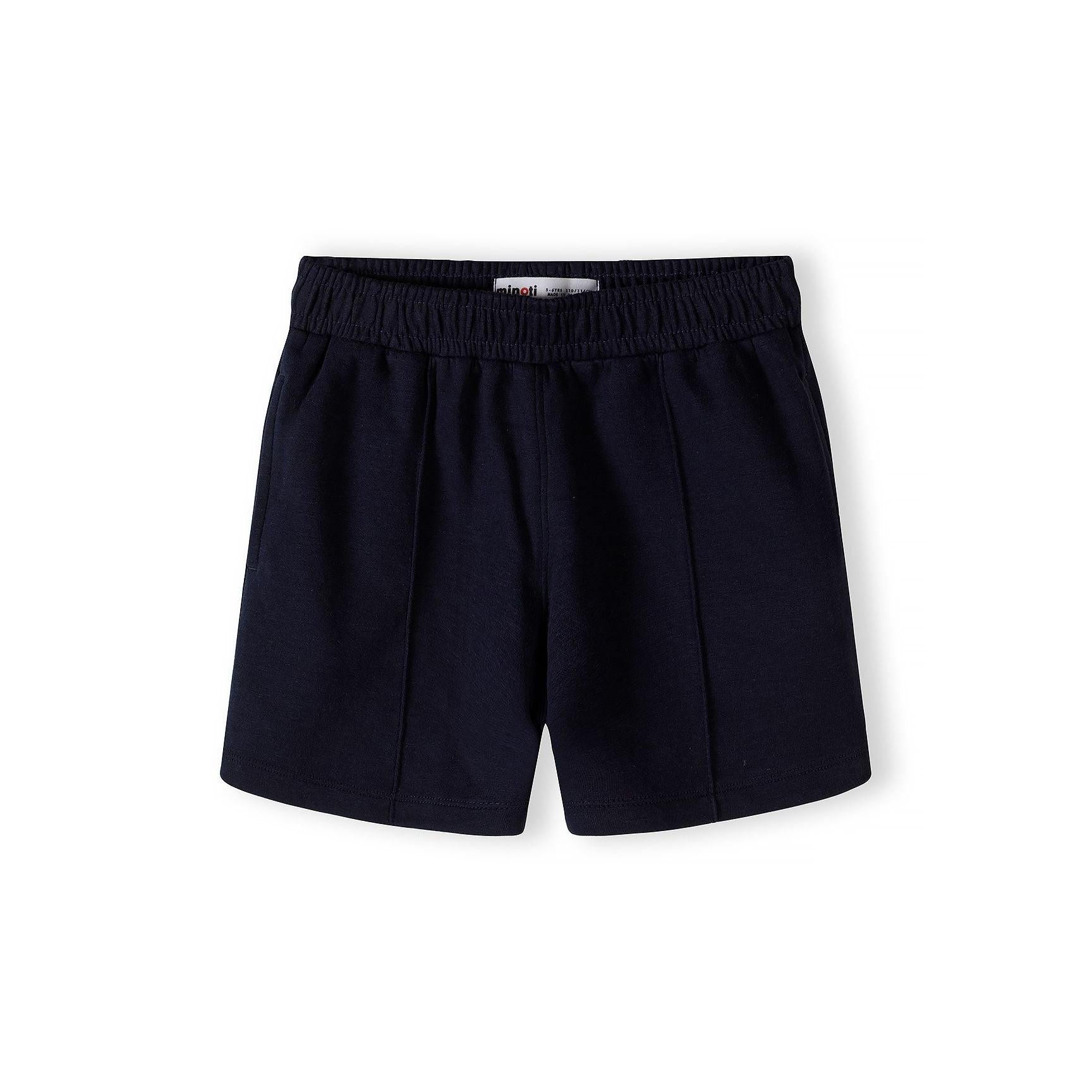 Close-up detail of cream pique polo shirt showing Minoti label, zip neck opening, navy collar and subtle embroidered logo on chest