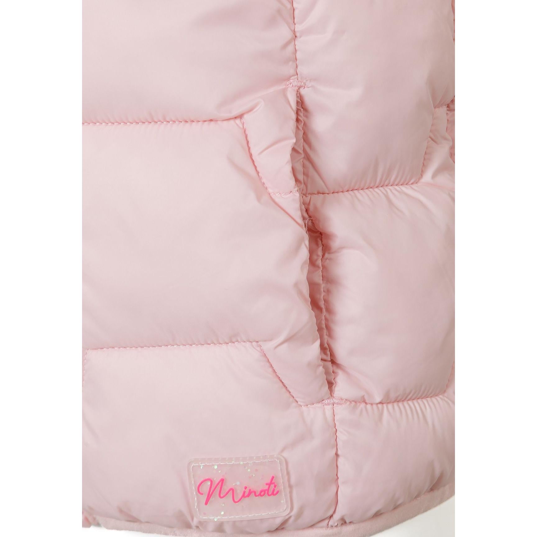 Young girl smiling wearing pink quilted gilet over beige tracksuit on light grey studio background