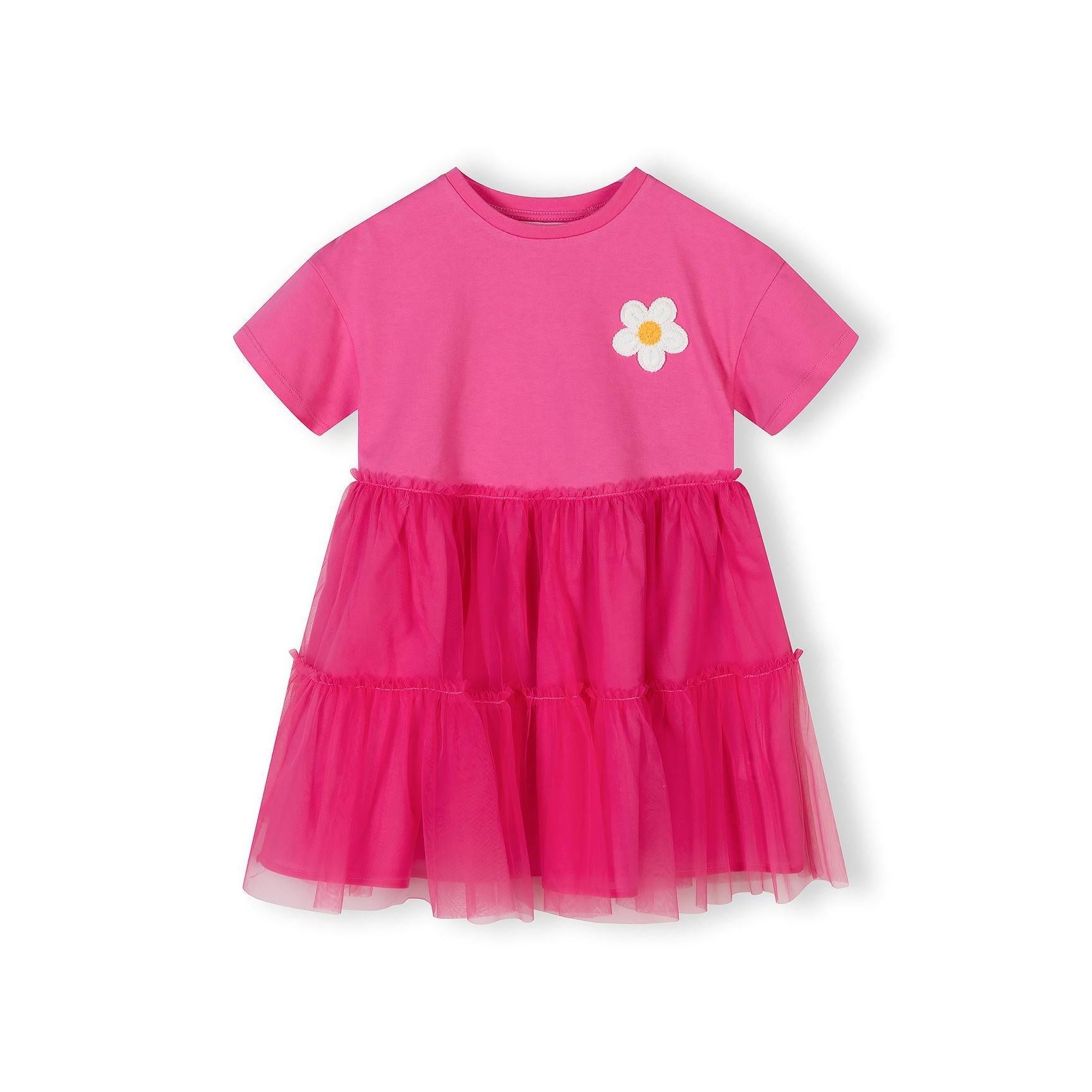 Pink jersey dress with short sleeves and layered tulle skirt, featuring white crochet flower appliqué on chest, displayed against white background
