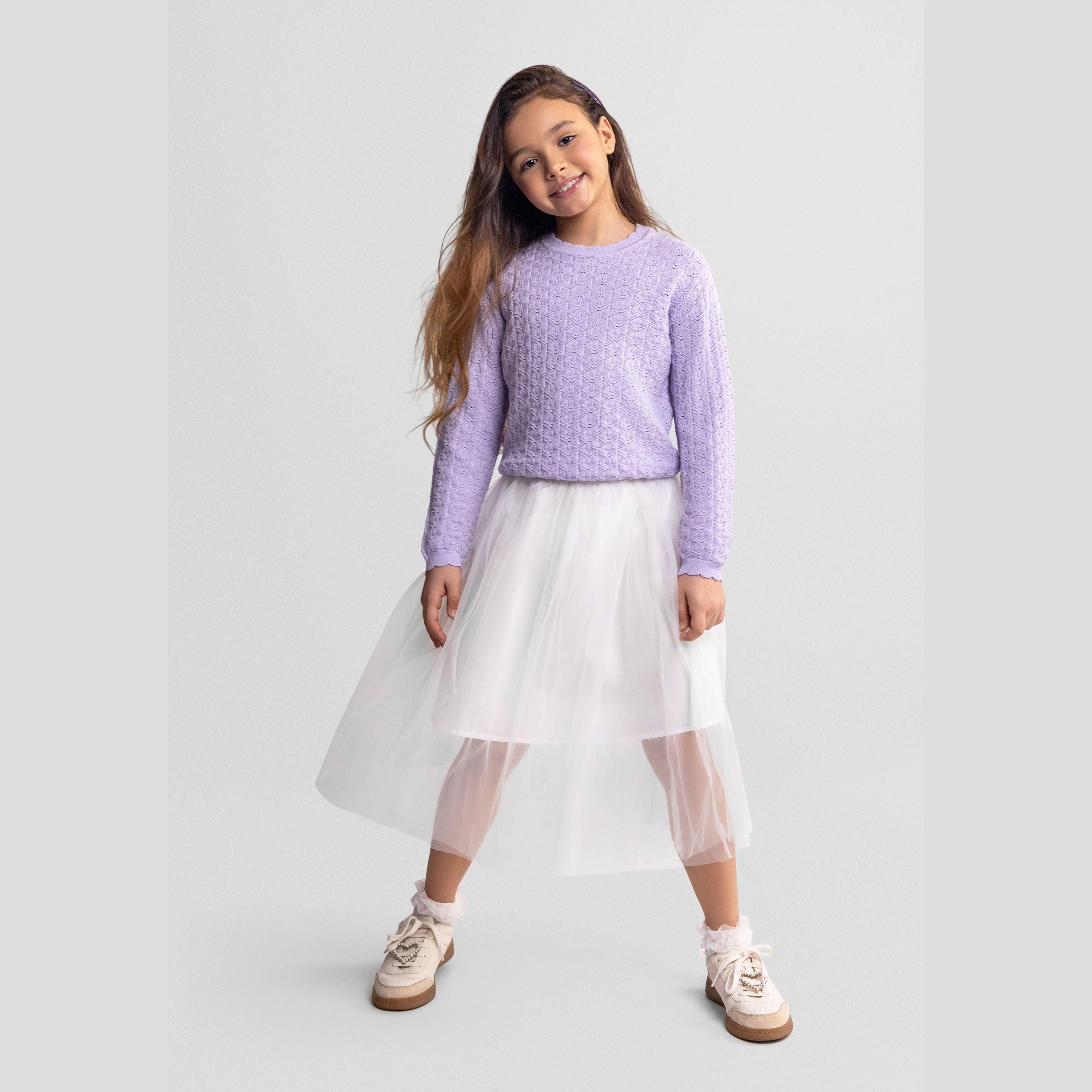 Young girl wearing lilac knitted jumper with diamond pointelle pattern paired with white tulle skirt and cream sneakers on grey background