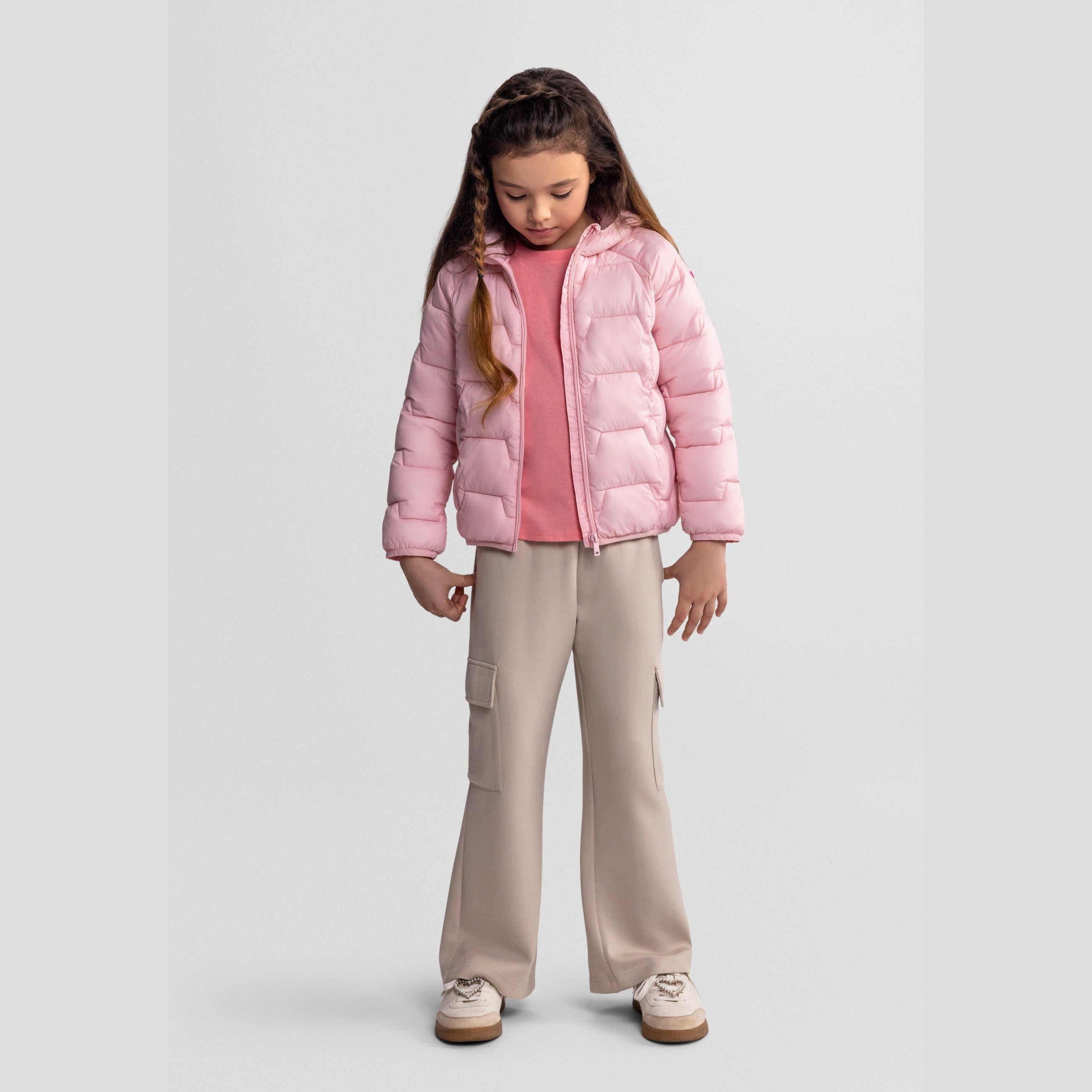 Girl in beige wide leg cargo joggers with pink puffer jacket and pink top, looking down with hands in pockets against white background