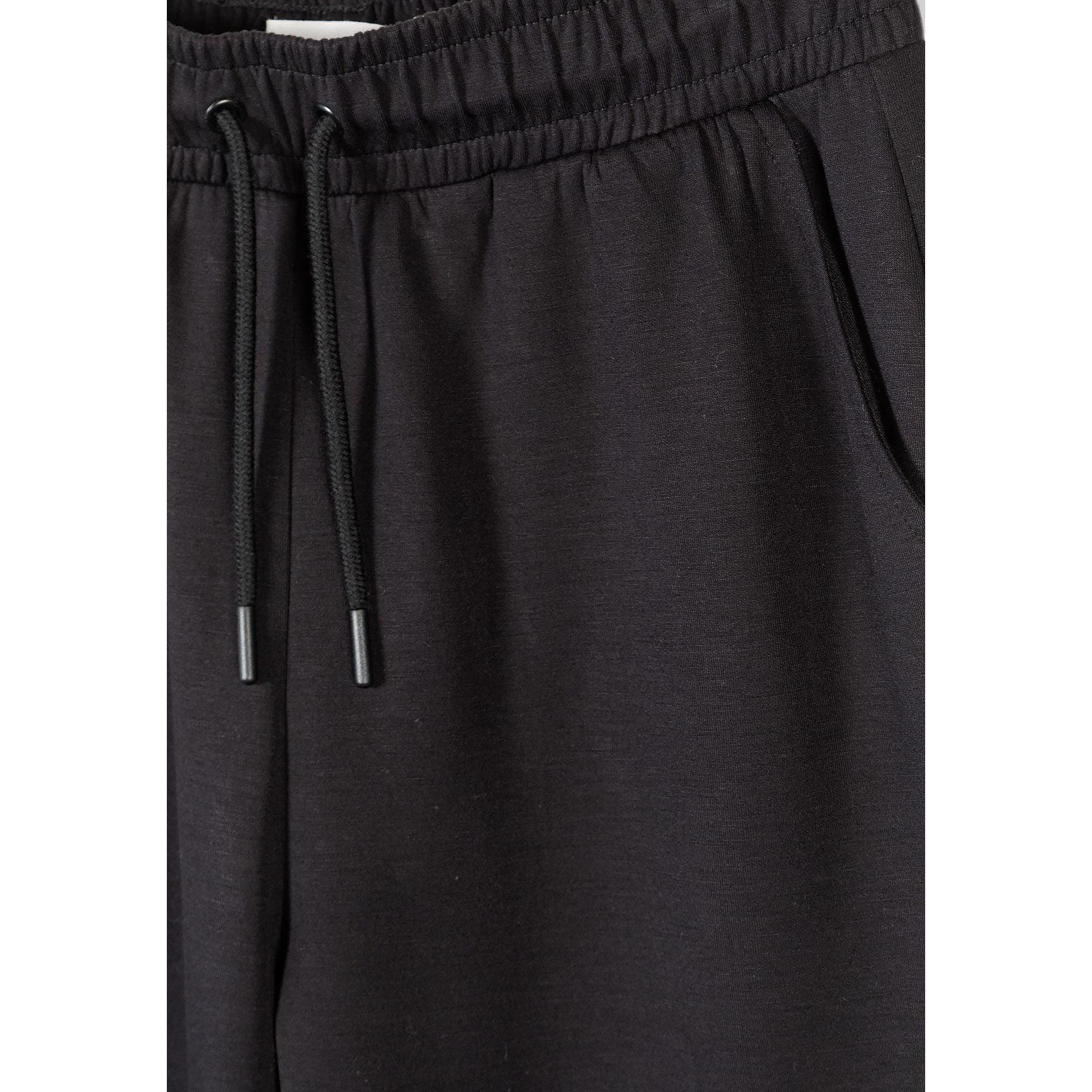 Close-up detail of black joggers showing elasticated waistband with drawstring and fabric texture