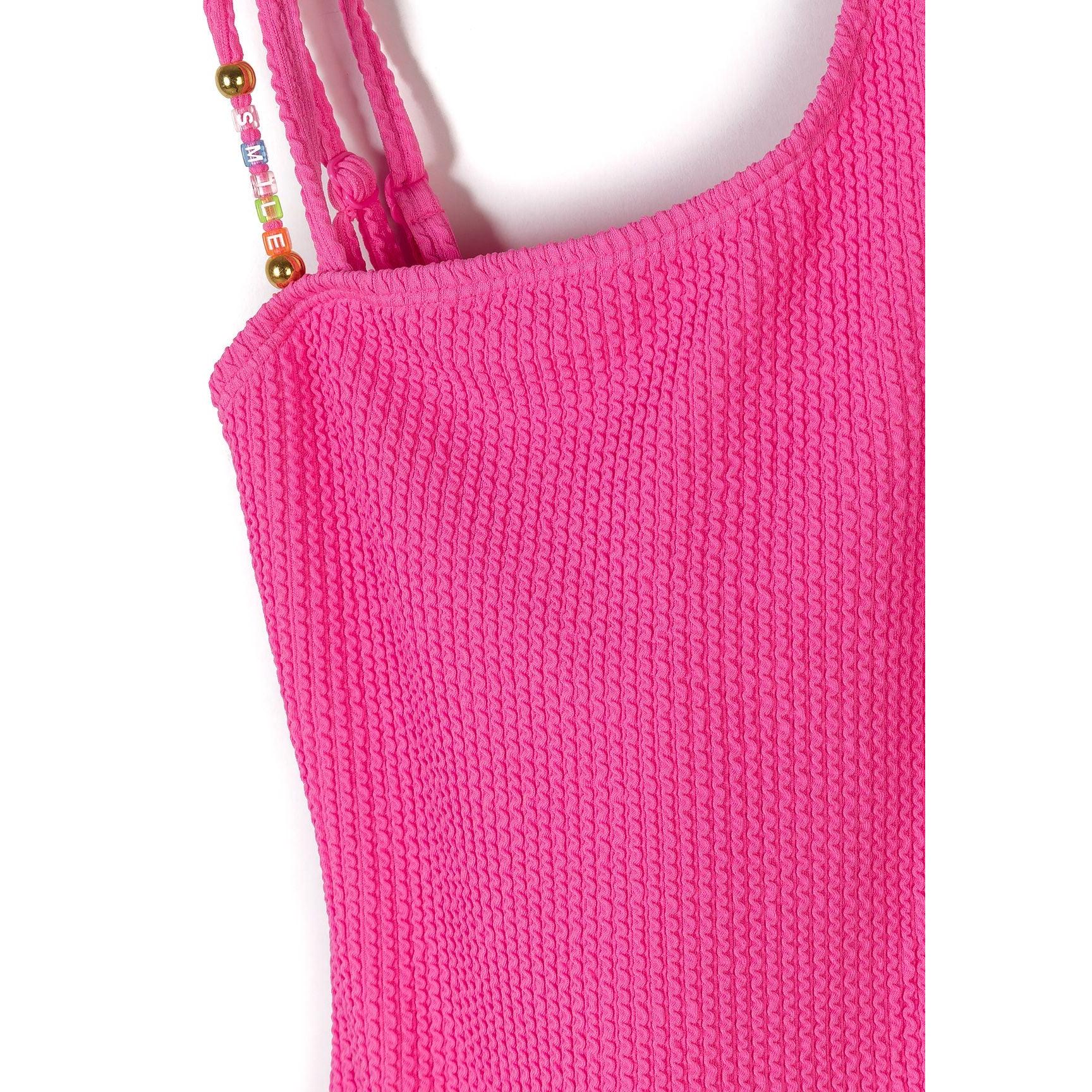Close-up detail of bright pink ribbed fabric texture and decorative beaded strap accent on white background