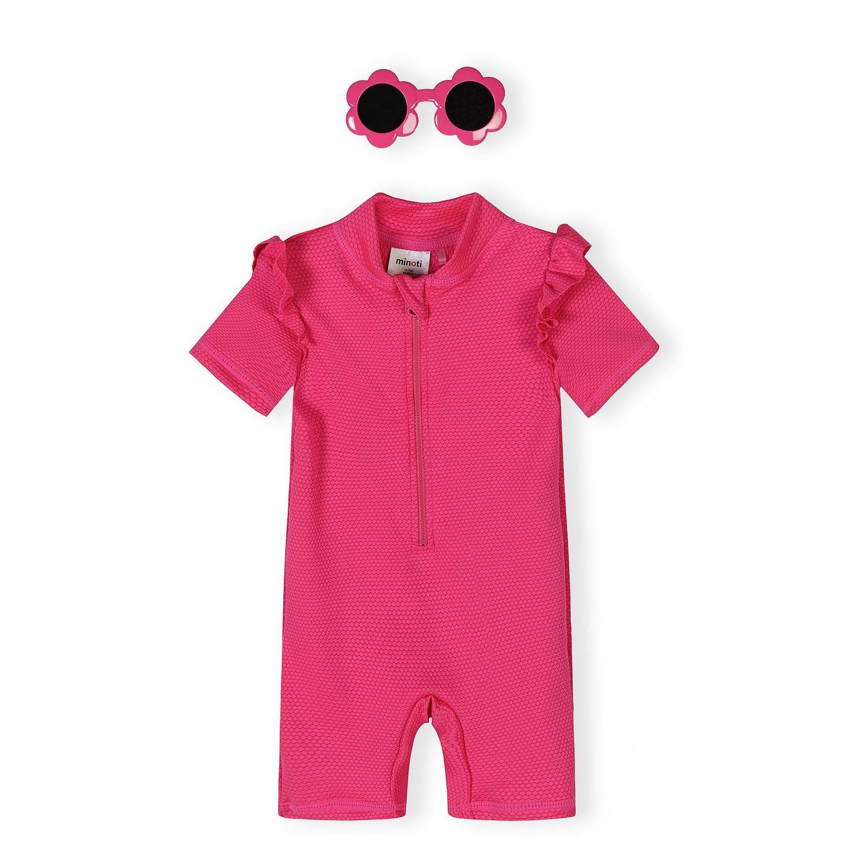 Pink textured rash suit with ruffle sleeves and flower-shaped sunglasses on white background, front view showing zip closure