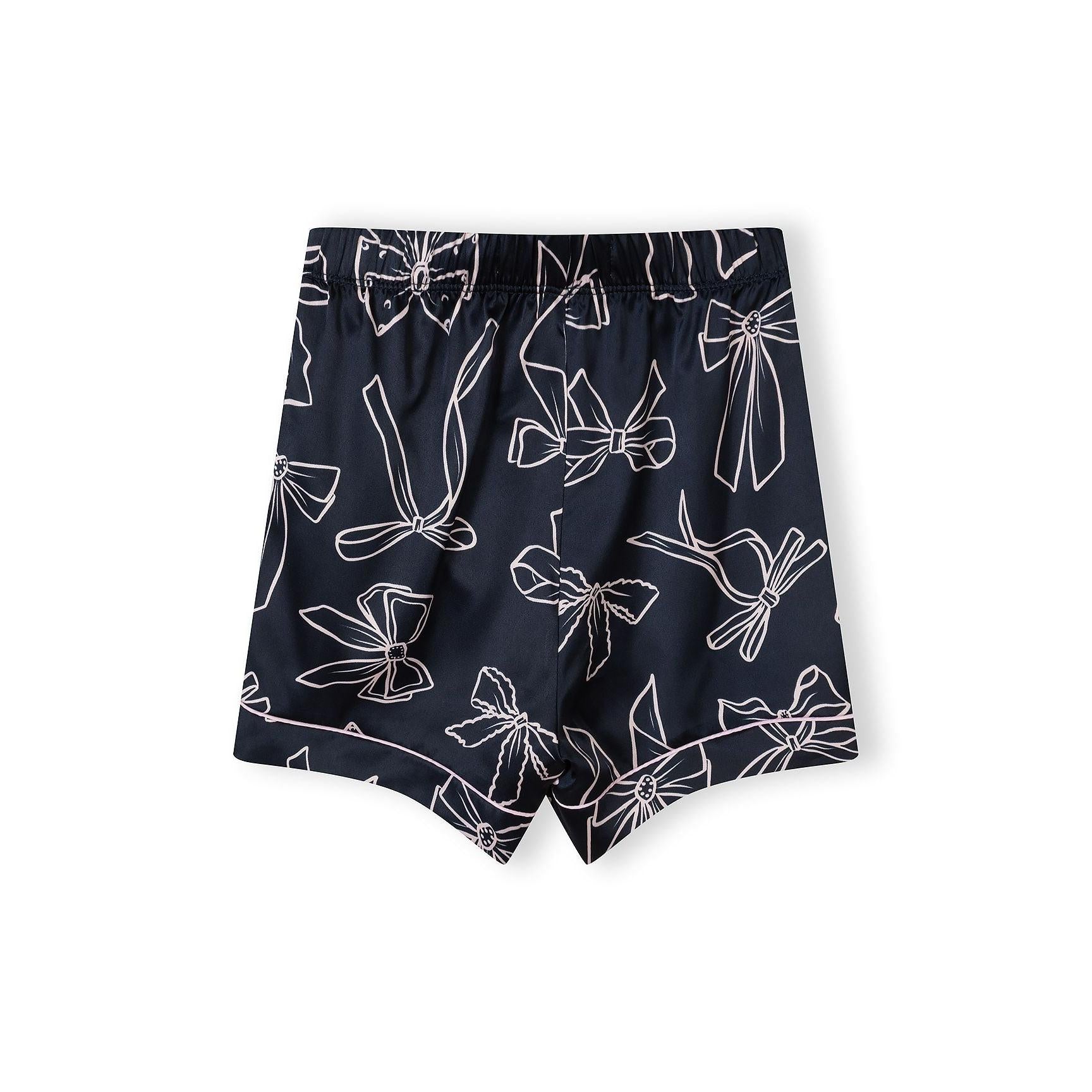 Detail view of navy satin pyjama top showing lapel collar, button placket, chest pocket and bow print pattern with Minoti label visible