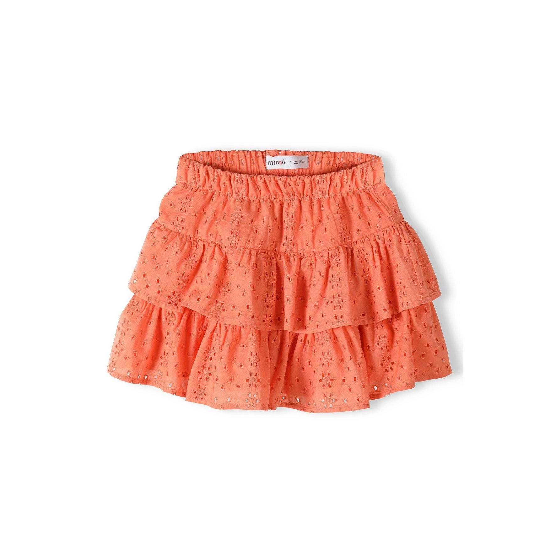 Coral broderie anglaise skirt with intricate embroidered holes and two-tier ruffle design laid flat on white background