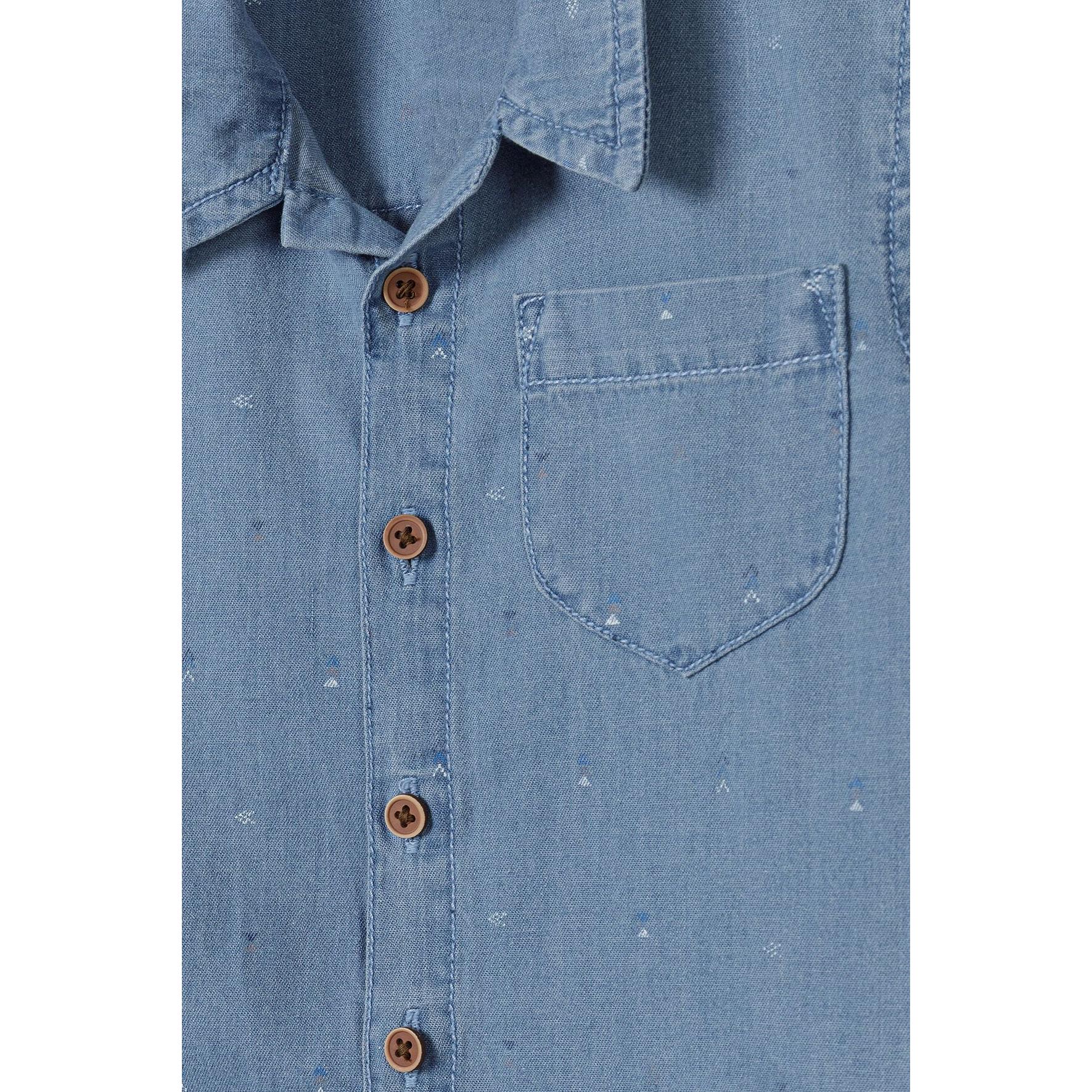 Close-up detail of light blue denim shirt showing brown buttons, chest pocket and speckled print pattern