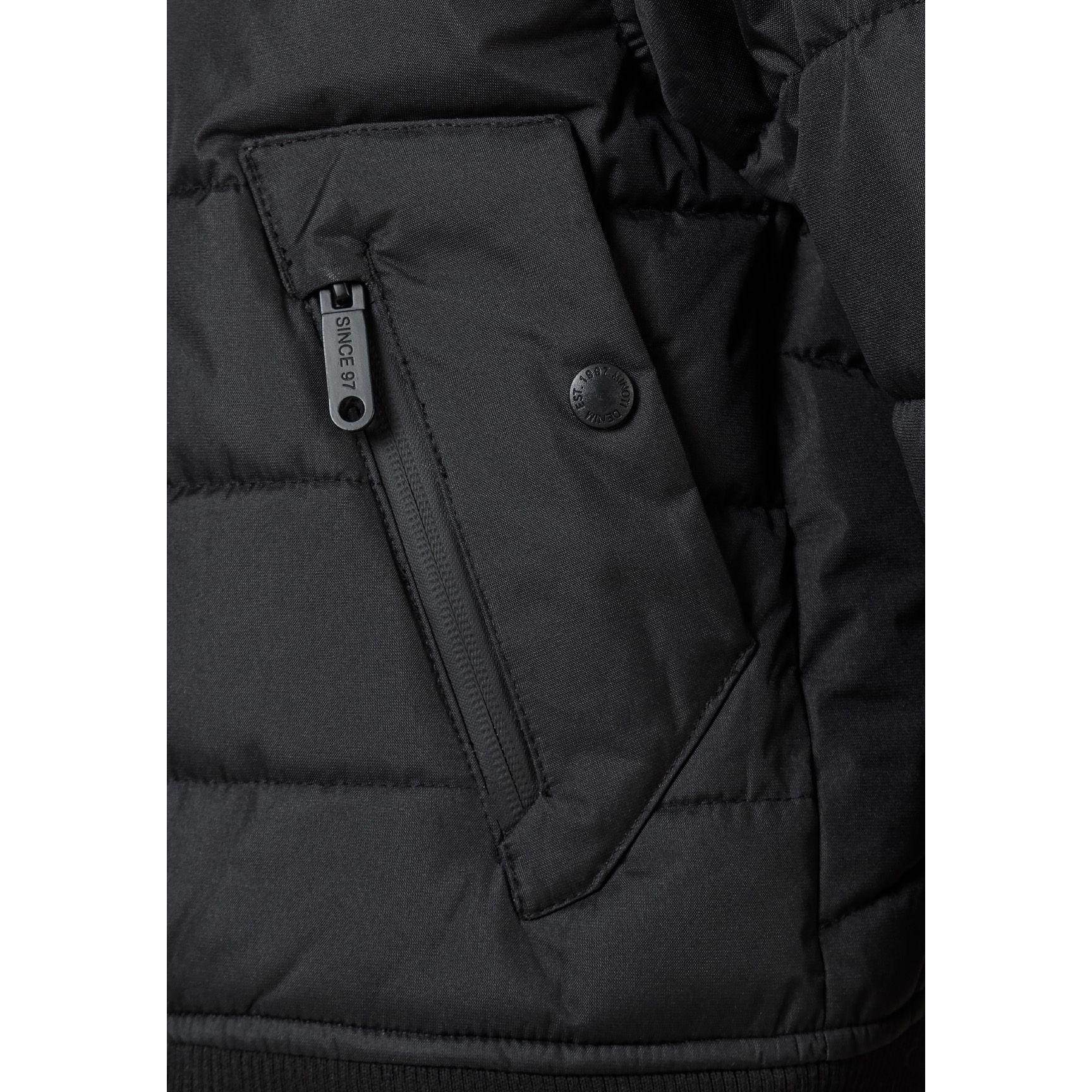 Close-up detail of black circular Minoti logo patch on the sleeve of the padded jacket showing MT 97 branding