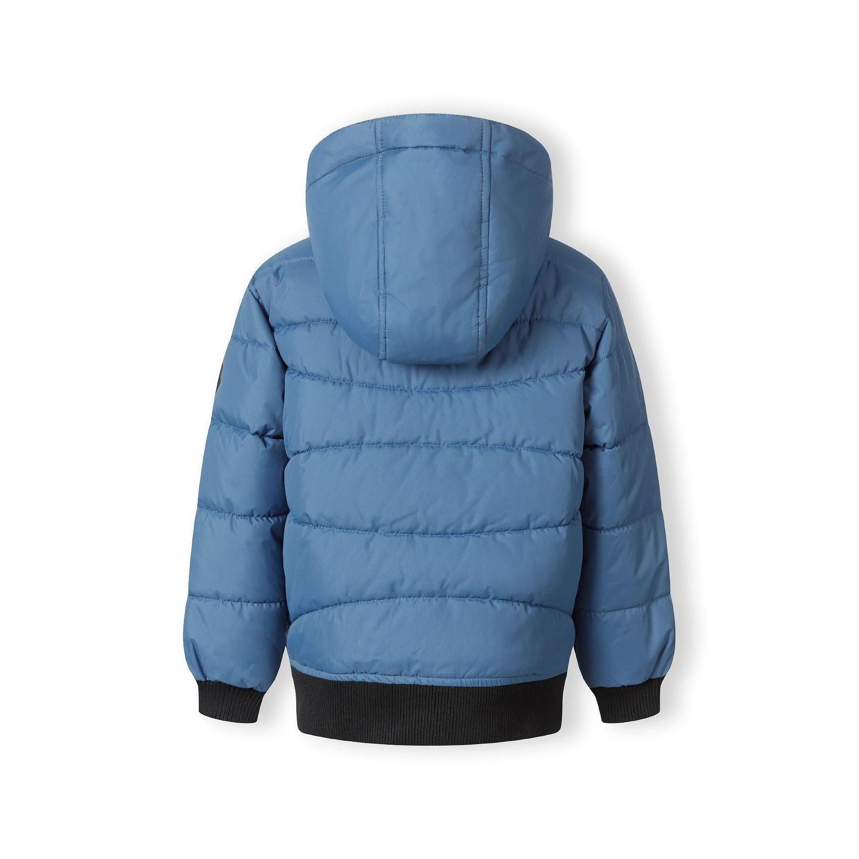 Close-up detail of blue padded jacket showing circular Minoti logo patch with cross design