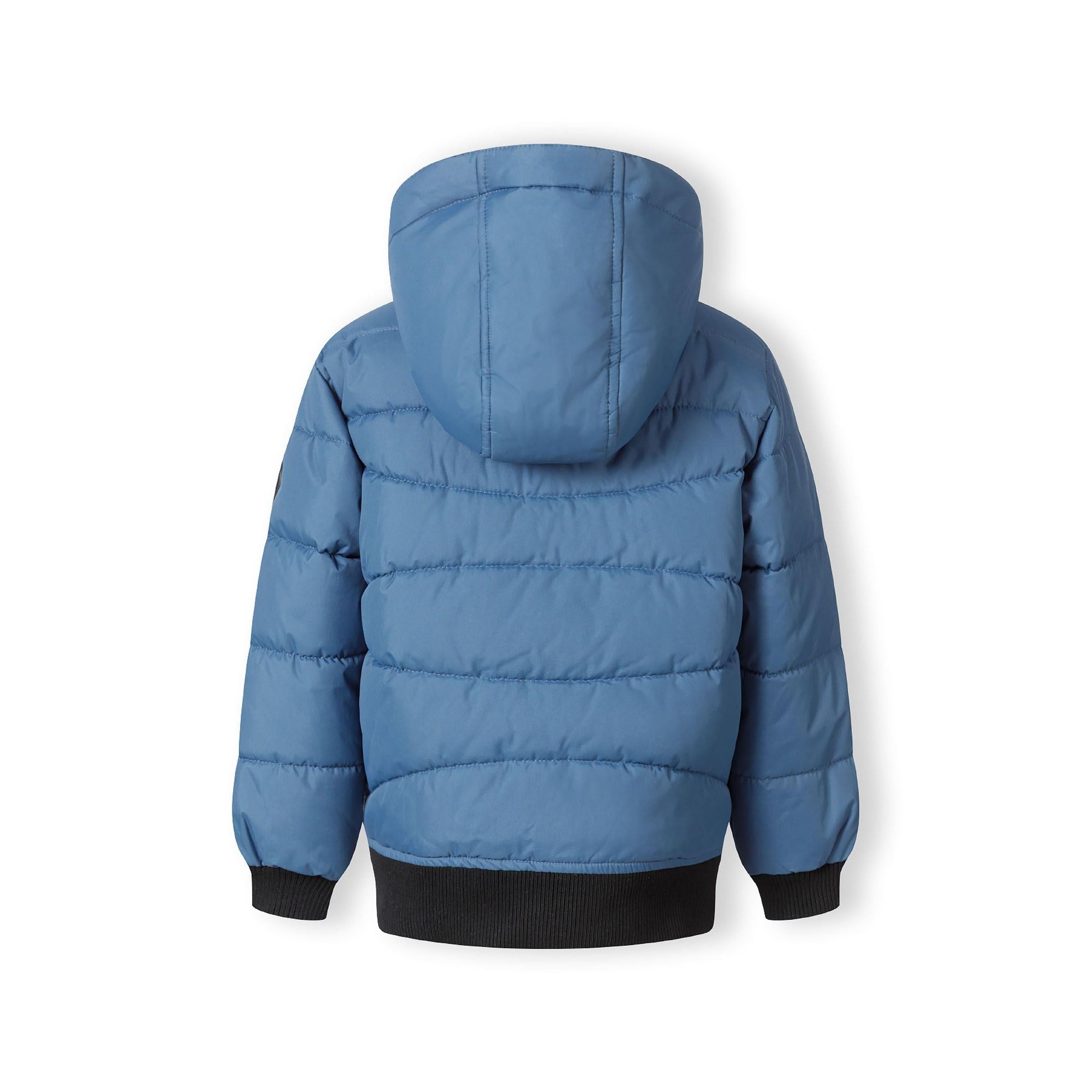 Close-up detail of blue padded jacket showing circular Minoti logo patch with cross design