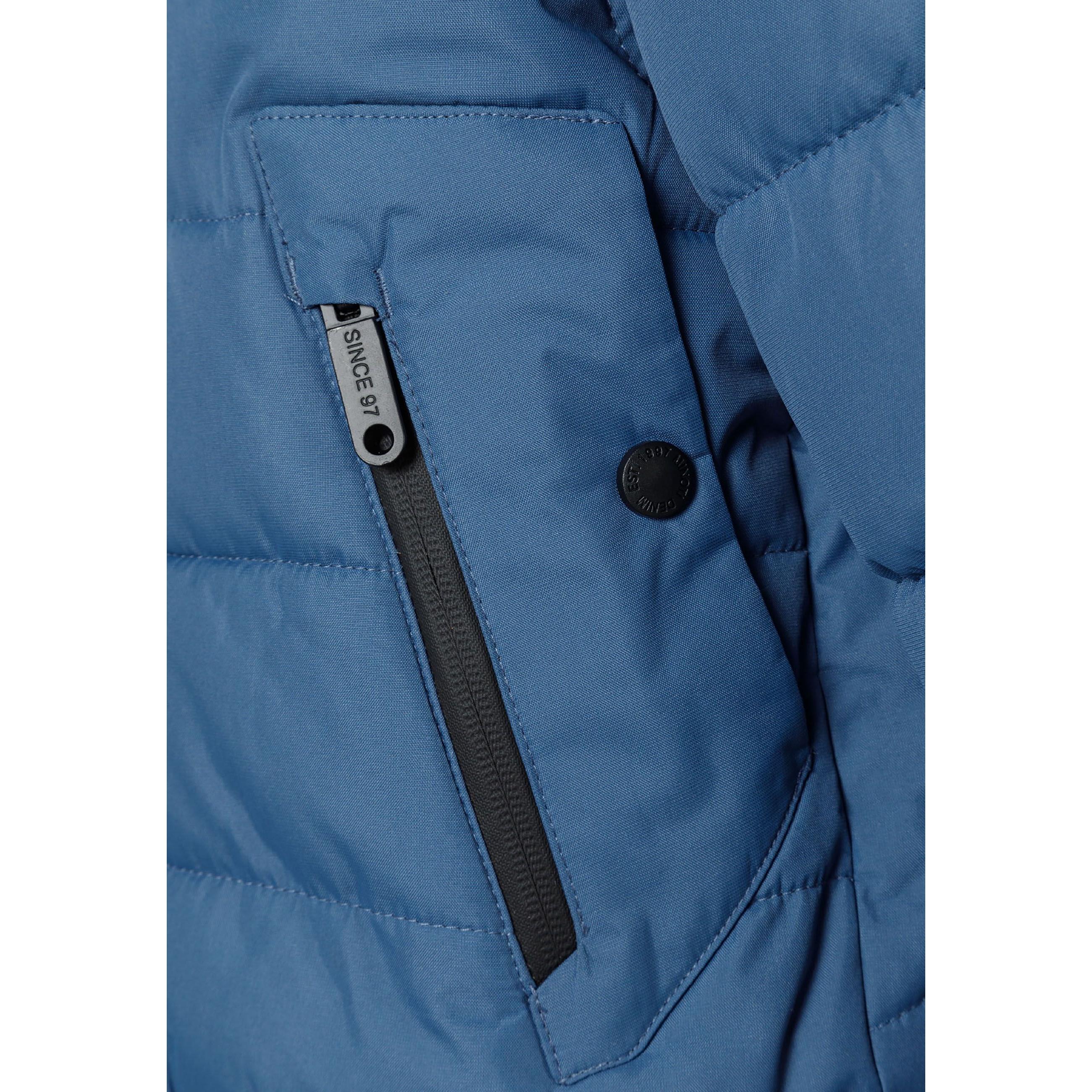 Close-up detail of blue padded jacket showing circular Minoti logo patch with cross design