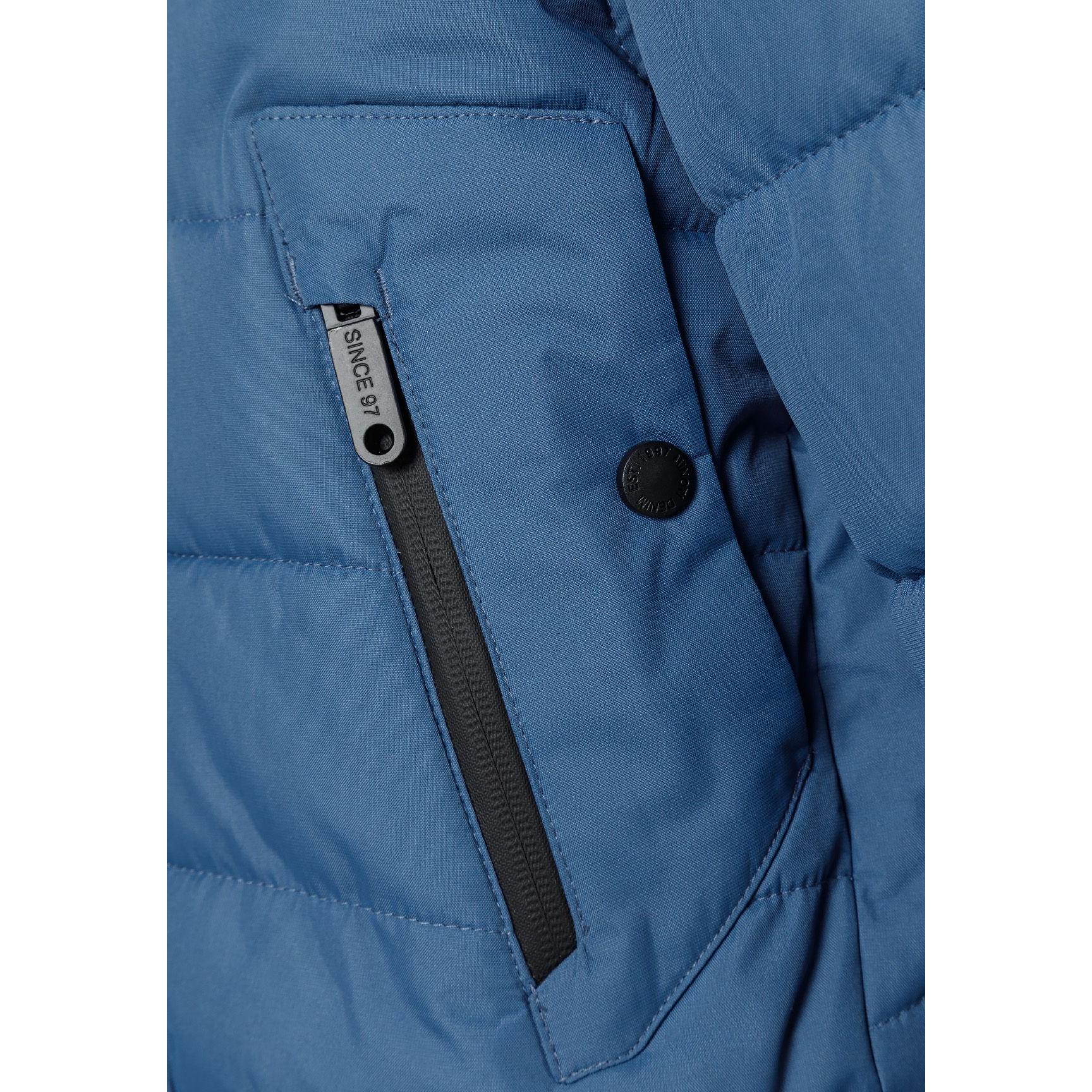 Close-up detail of blue padded jacket showing circular Minoti logo patch with cross design