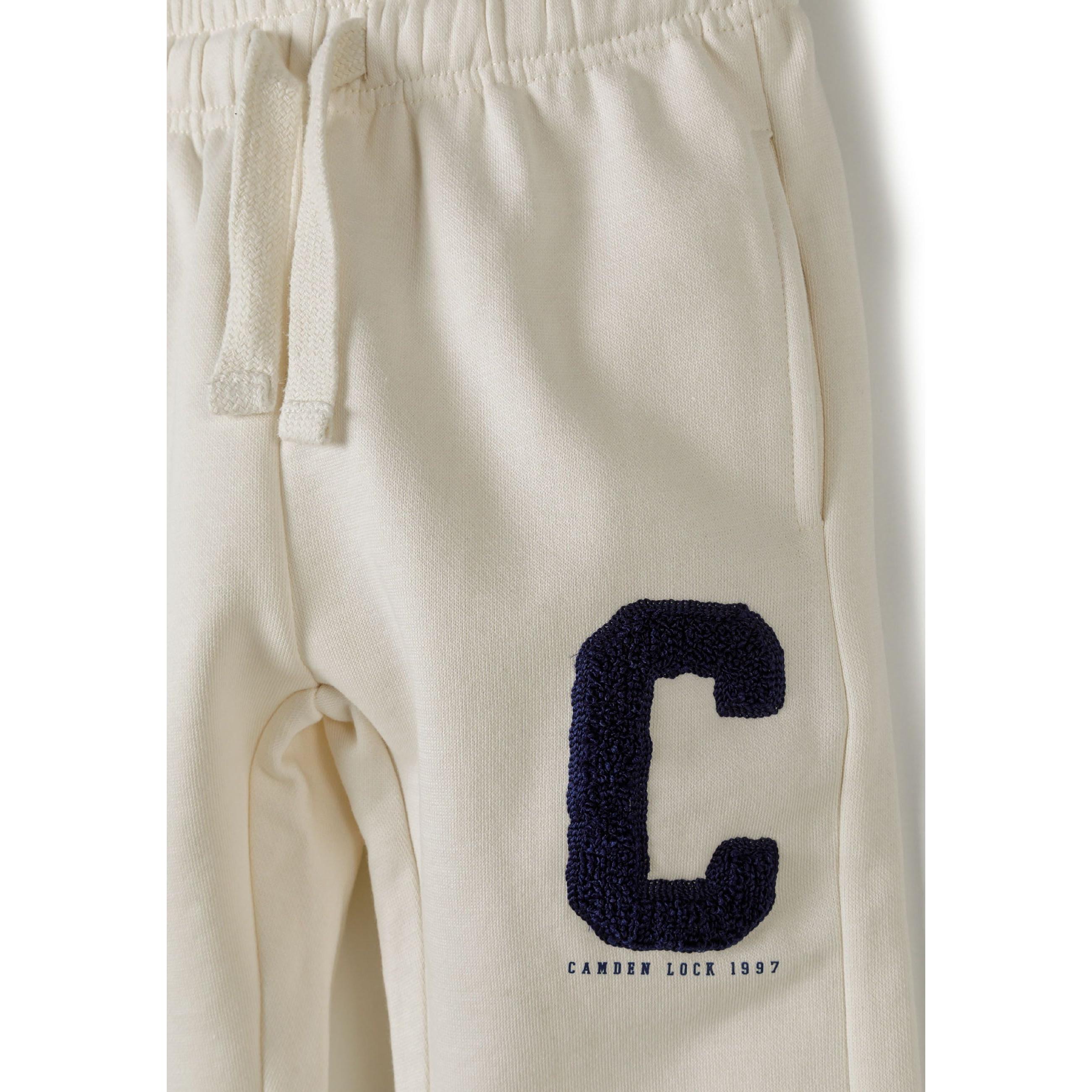 Close-up detail of cream joggers showing large navy blue C boucle embroidery and drawstring waistband