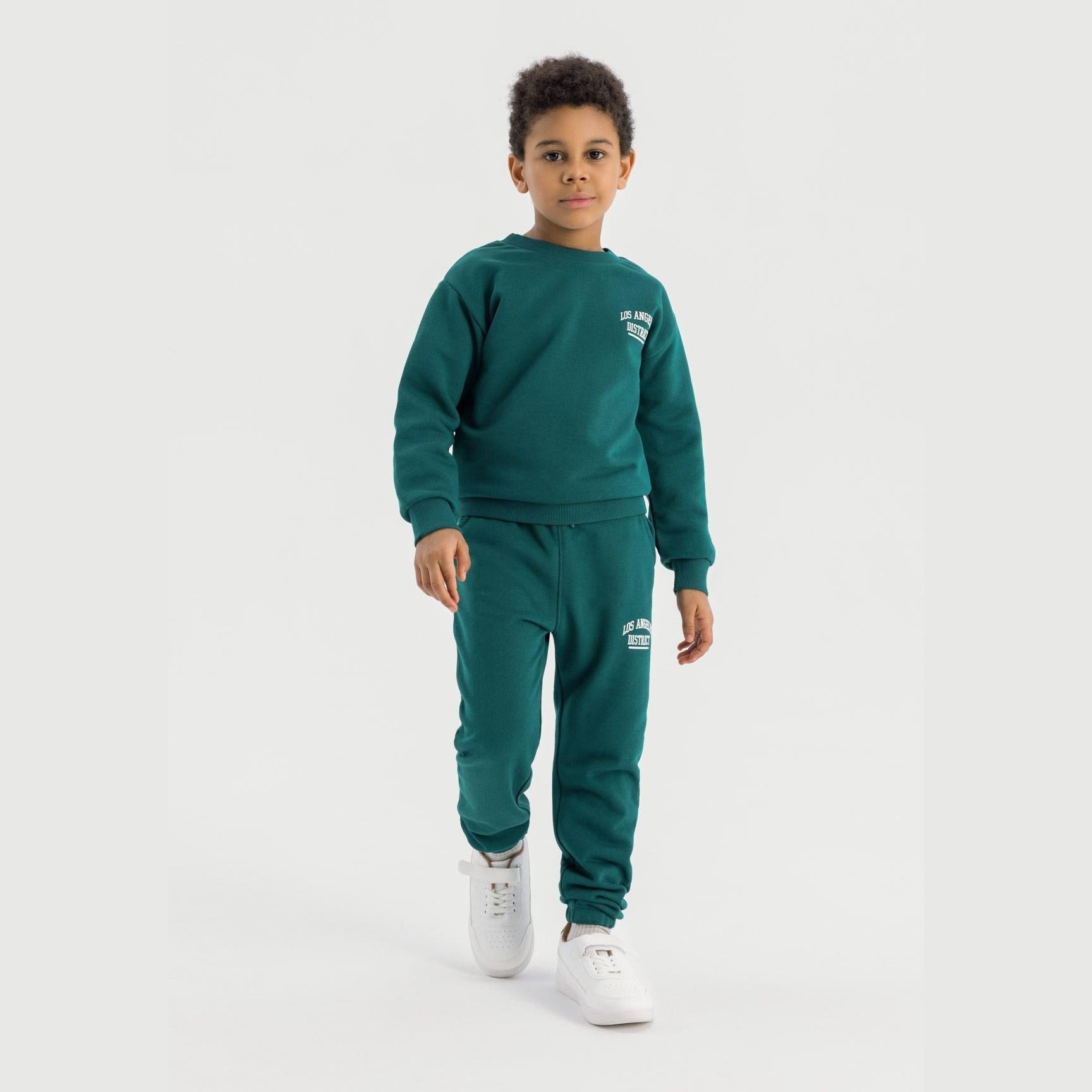 Boy wearing dark green crew neck sweatshirt and matching joggers set with Los Angeles District branding, standing against white background