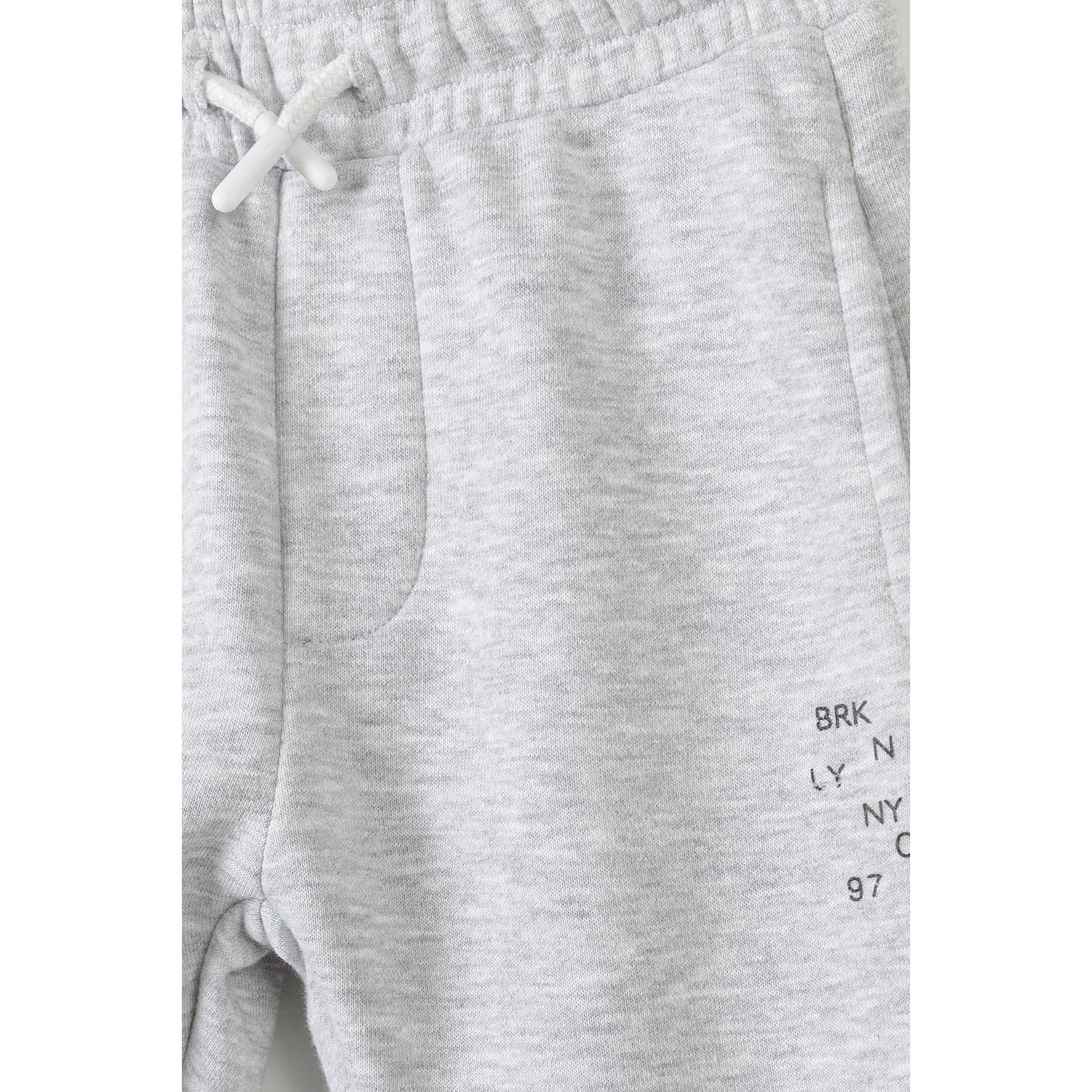 Close-up detail of grey fleece joggers showing Brooklyn print with BRK LY N NYC 97 text on front leg and drawstring waistband ties