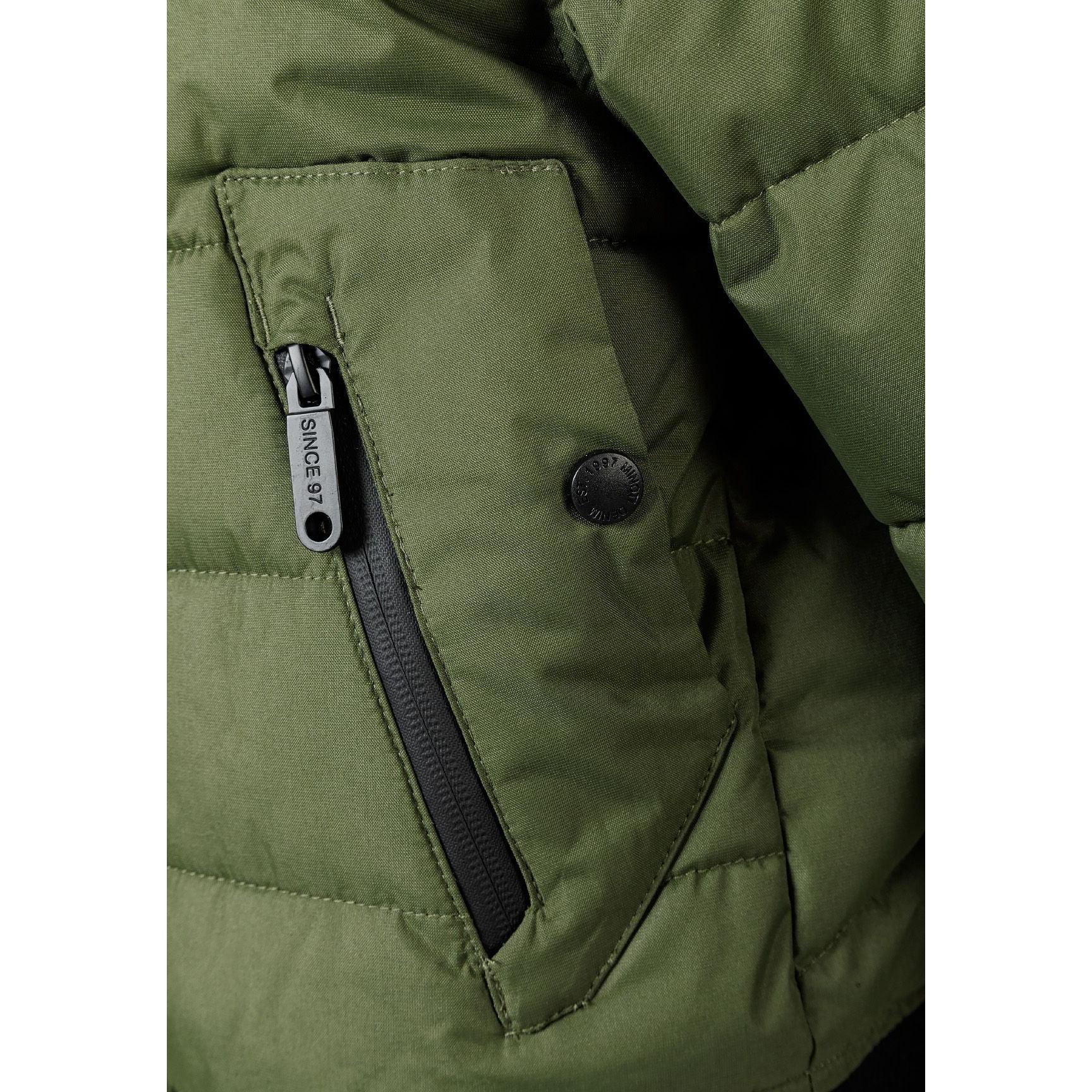 Close-up detail of khaki padded jacket showing circular black Minoti brand badge with crossed design and number 97