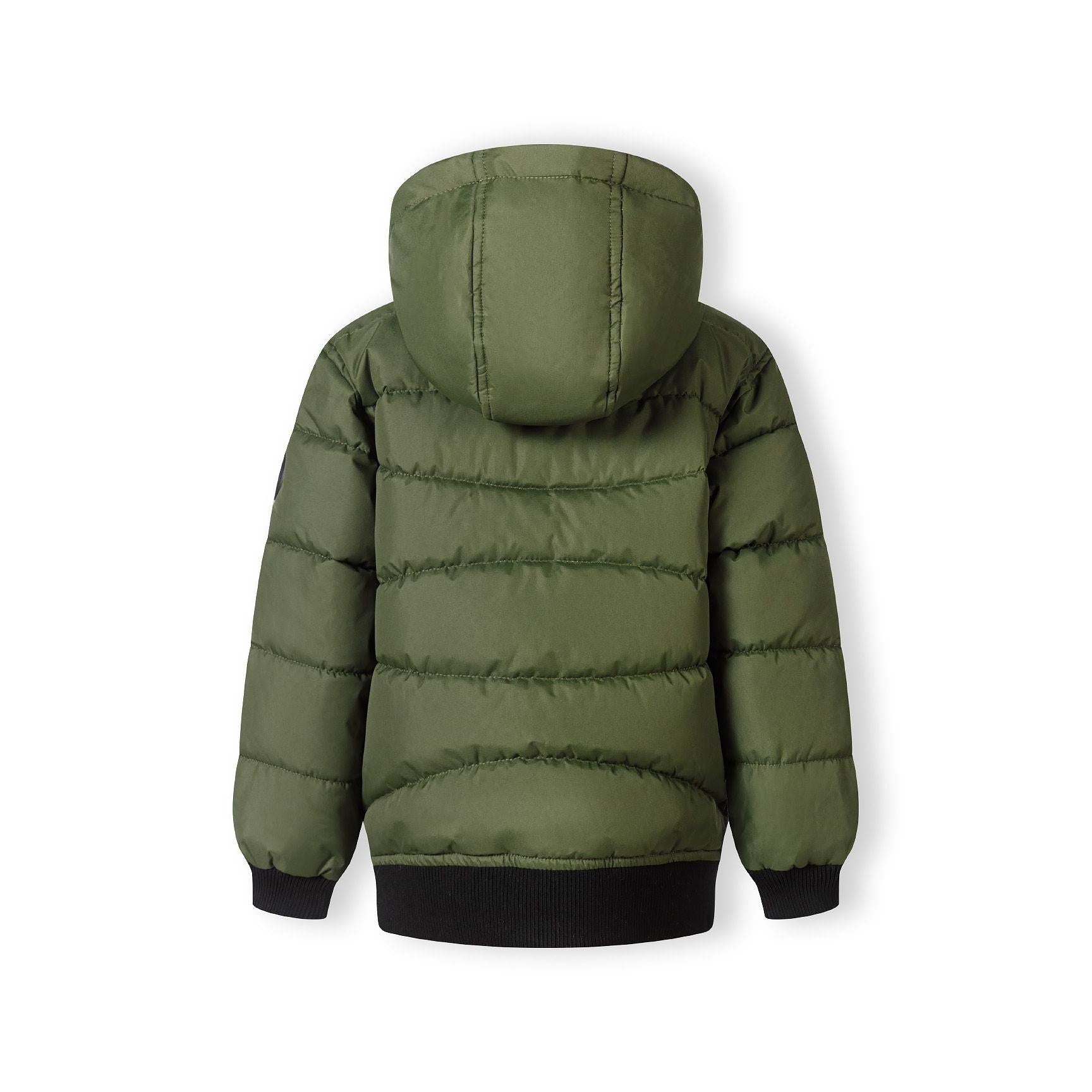 Close-up detail of khaki padded jacket showing circular black Minoti brand badge with crossed design and number 97