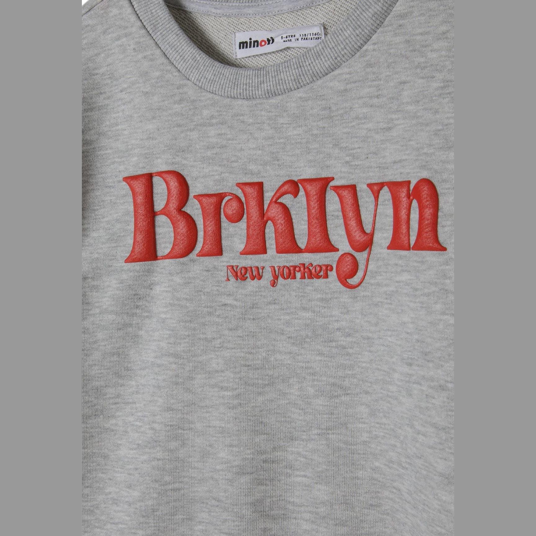 Close-up detail of grey sweatshirt showing red Brooklyn New Yorker text print and Minoti brand label at neckline