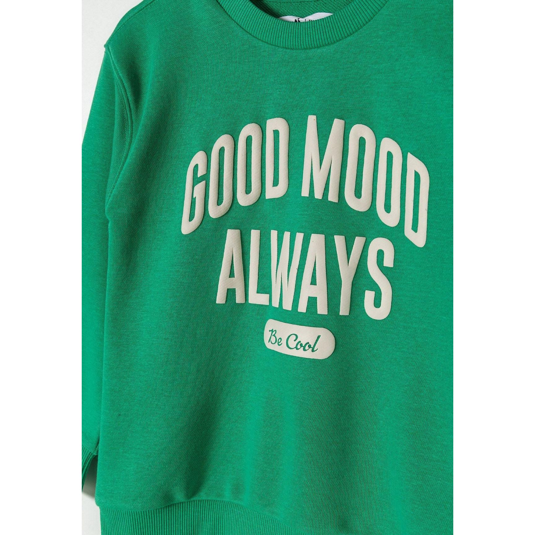 Close-up detail of bright green sweatshirt showing Good Mood Always Be Cool white print on chest area with soft cotton texture visible