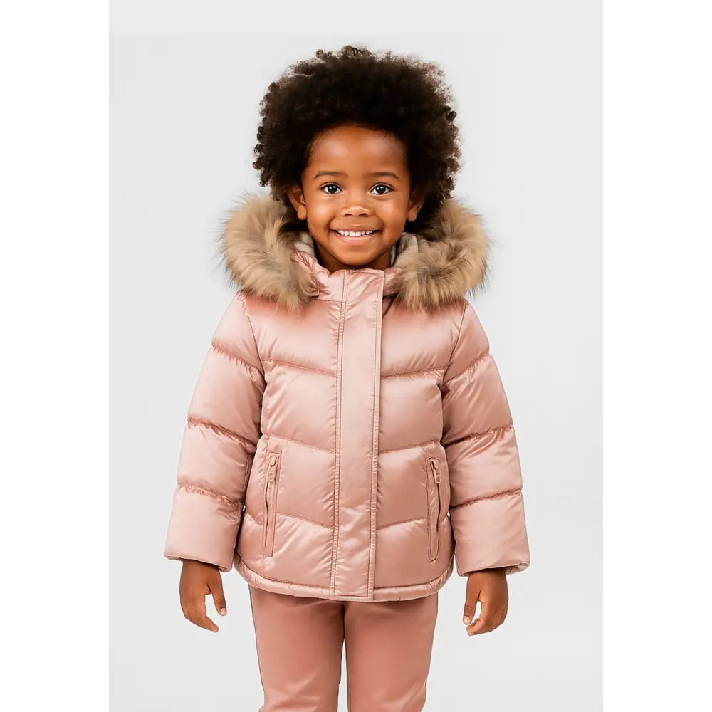 Young girl wearing metallic pink quilted winter jacket with faux fur hood trim, standing against white background