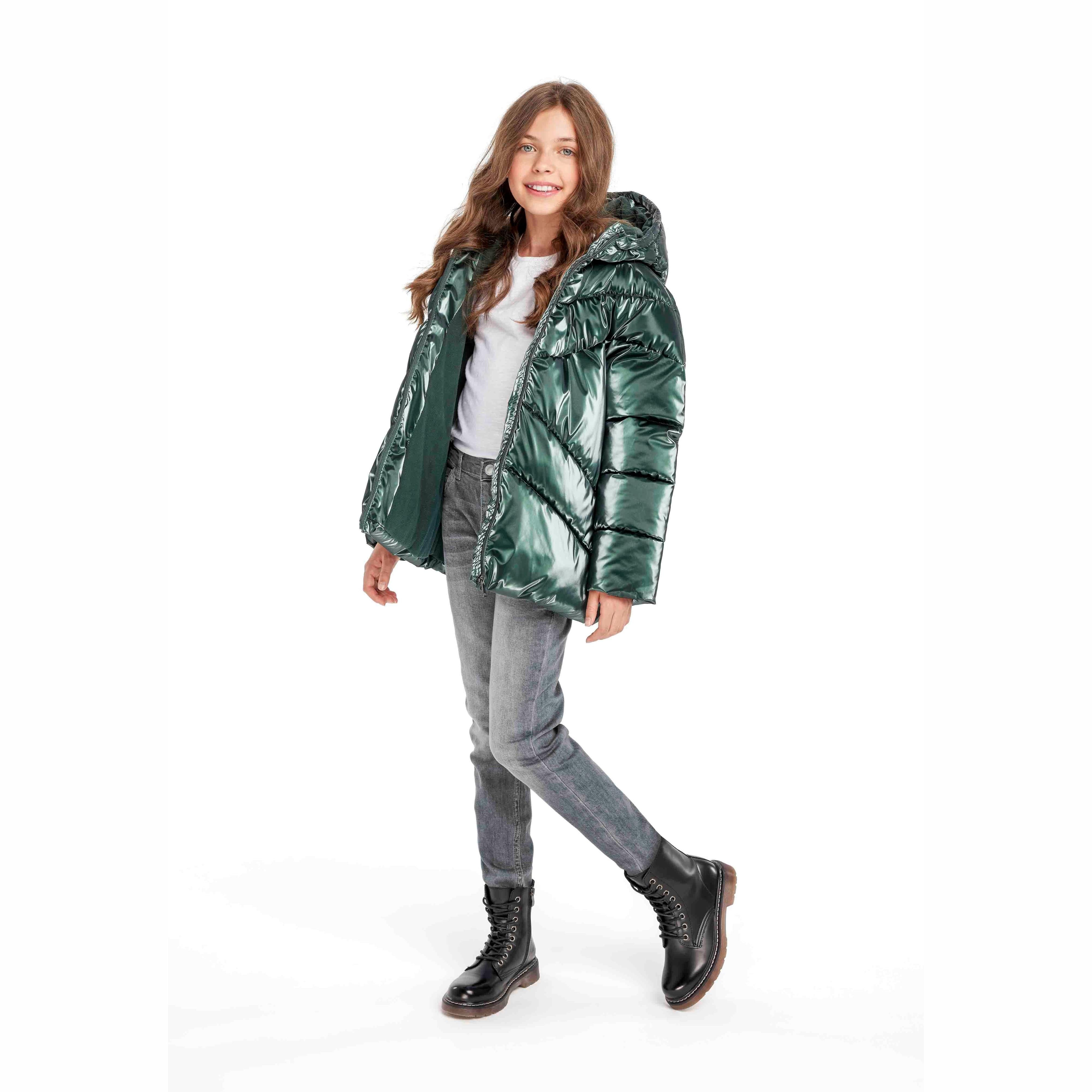 Girl wearing metallic dark green padded jacket with fur hood, styled with grey jeans and black boots on white background